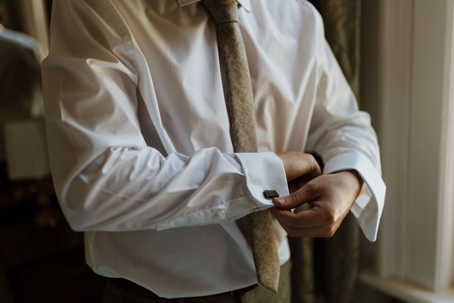 Detailed shot of groom putting on cufflinks on wedding day