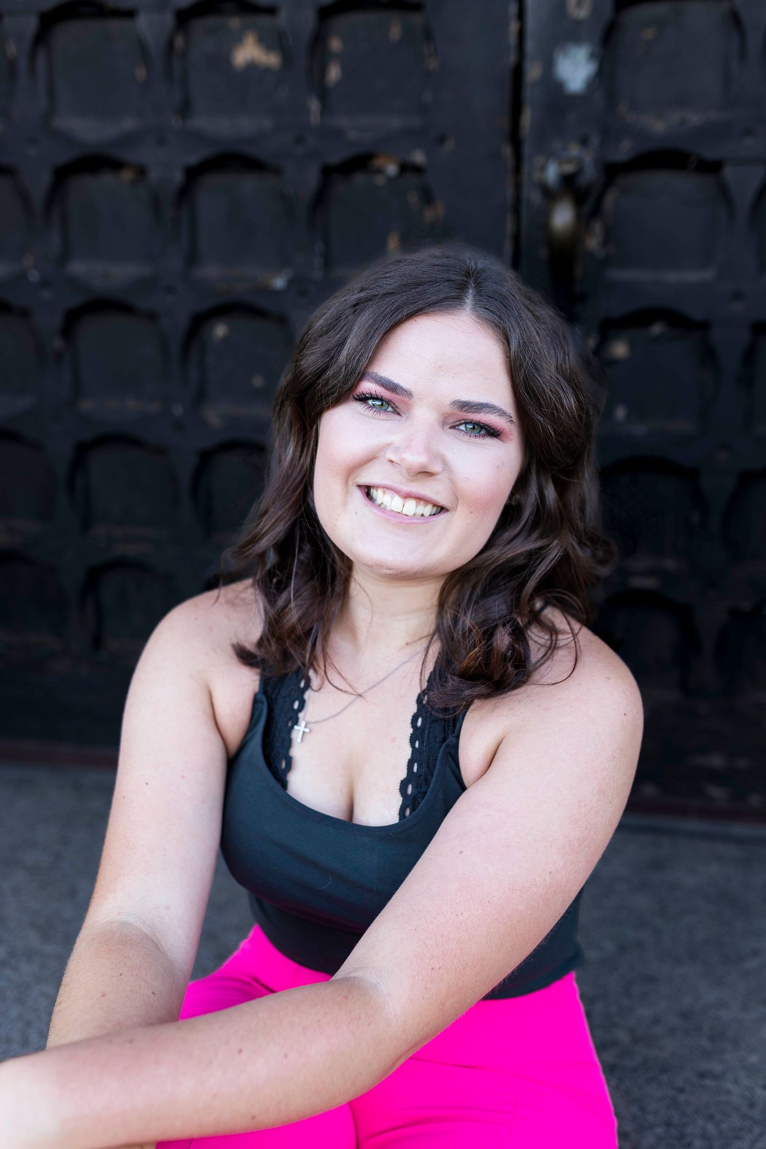 A candid portrait against a dark textured wall wearing a black top and pink bottoms.