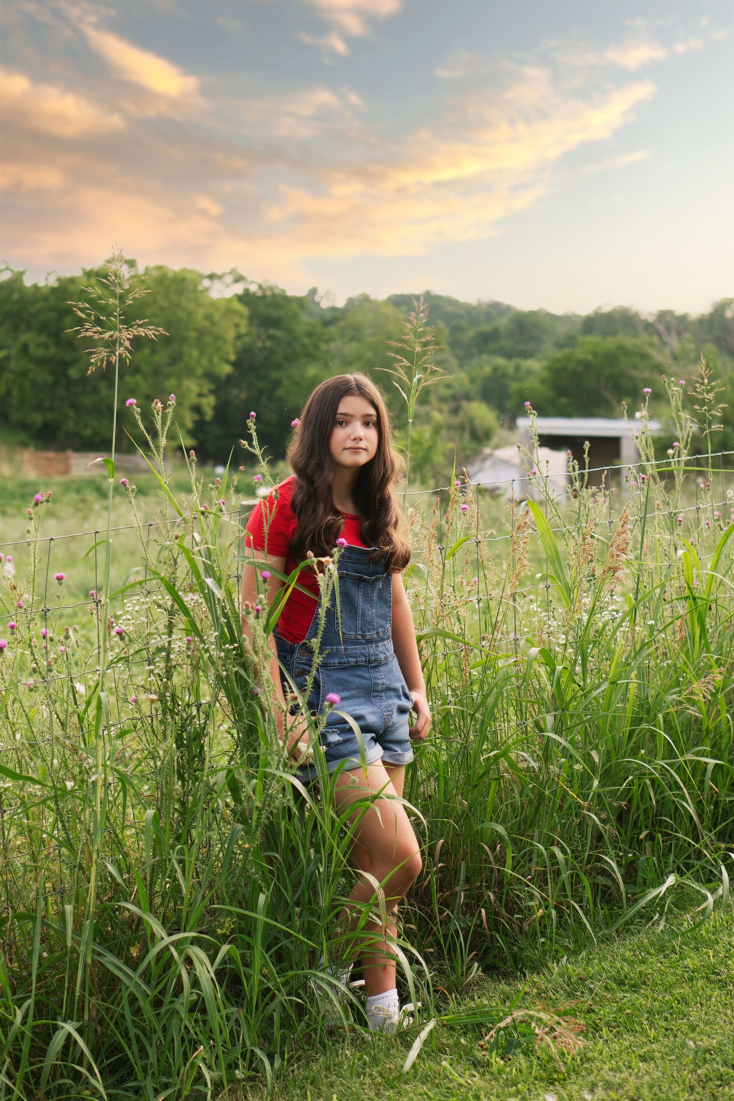 teen girl leans against fence post in country setting
