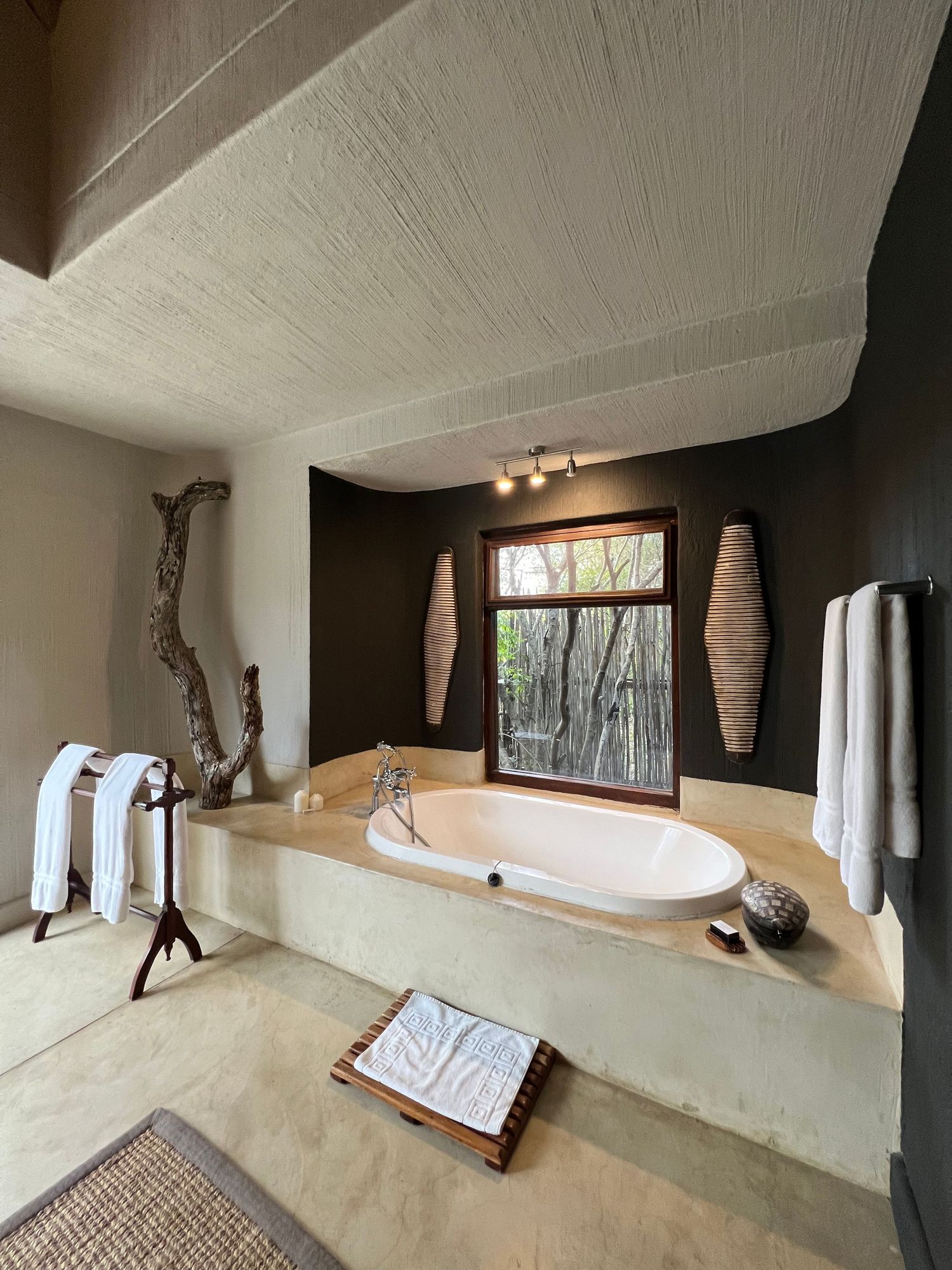 Luxury bathroom with built-in oval tub, natural wood accents, and picture window overlooking wilderness.