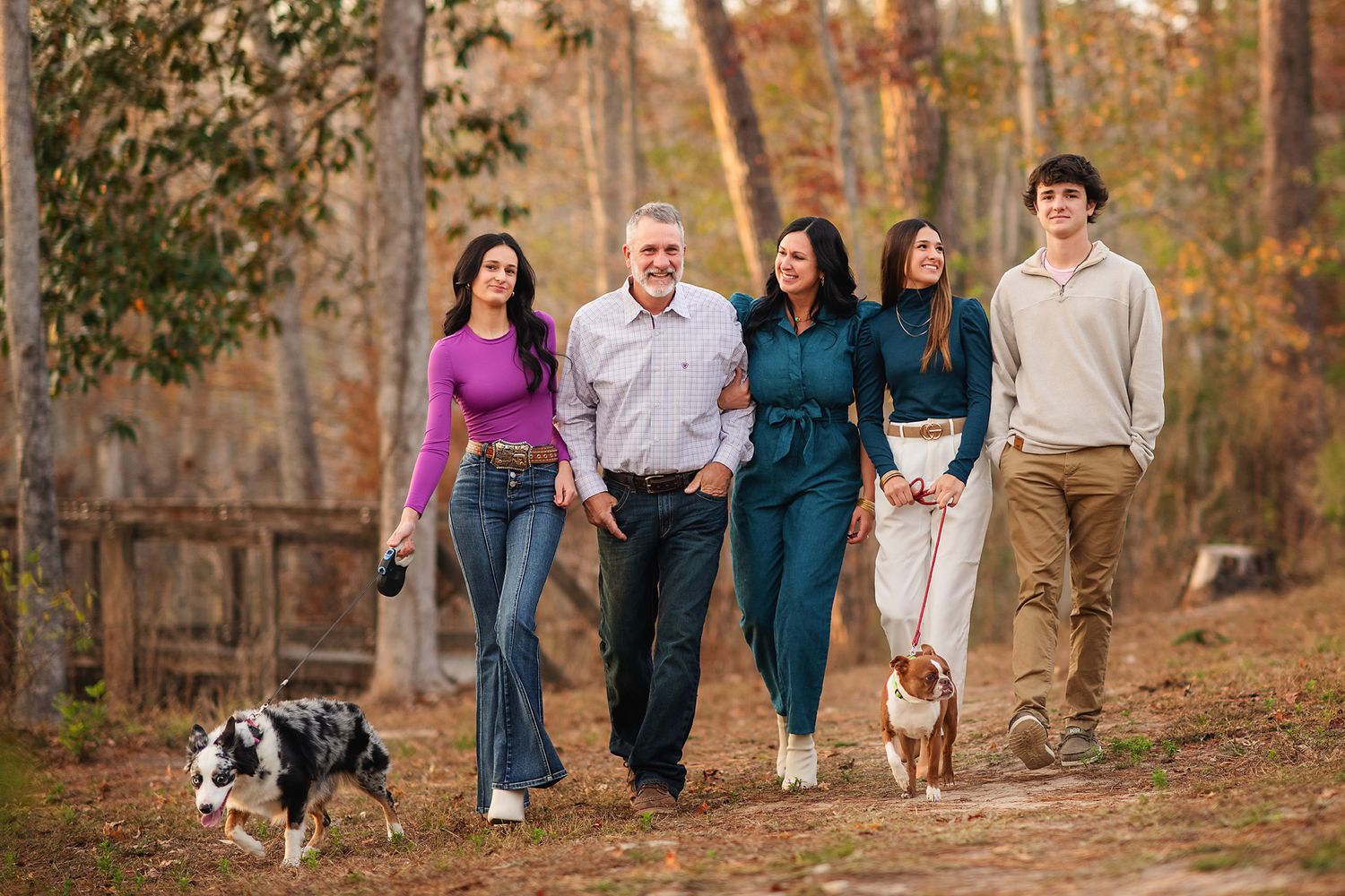 Happy family of five walking two dogs along a scenic autumn woodland path together.
