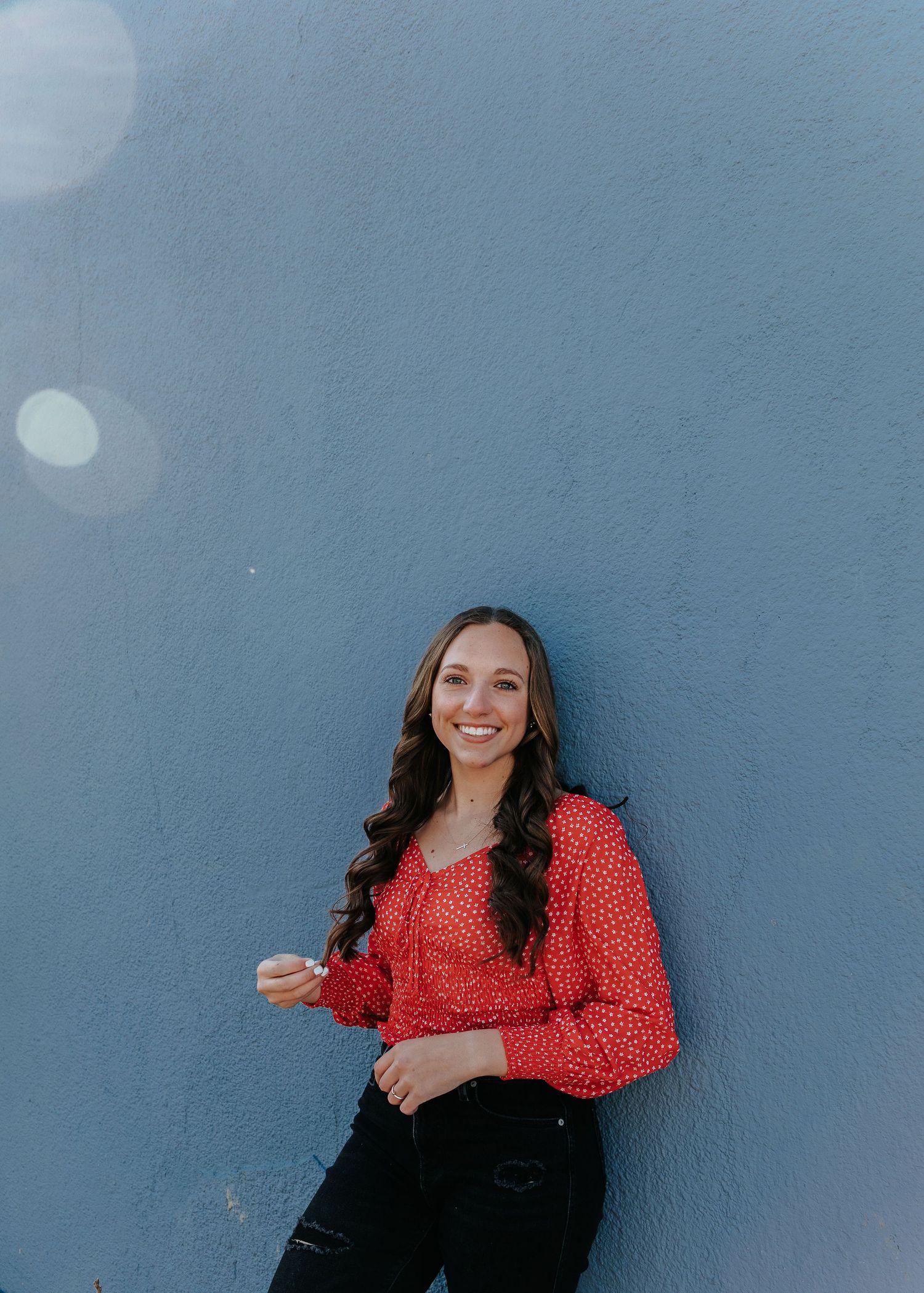 A stylish outfit with red polka dot blouse and black jeans against a blue wall background.