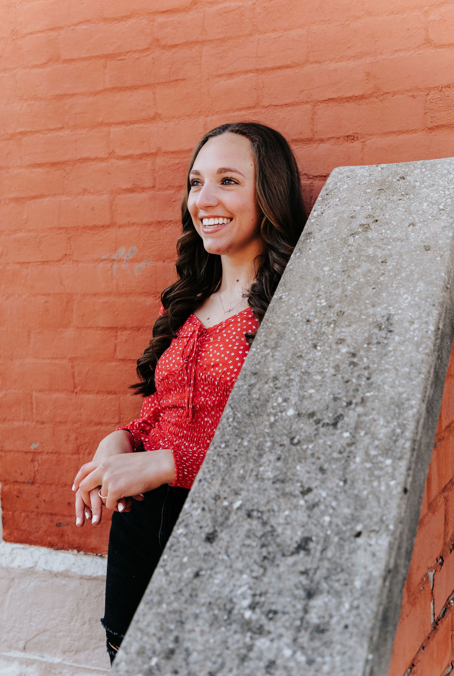 A casual portrait against a red brick wall wearing a polka dot top and dark pants.