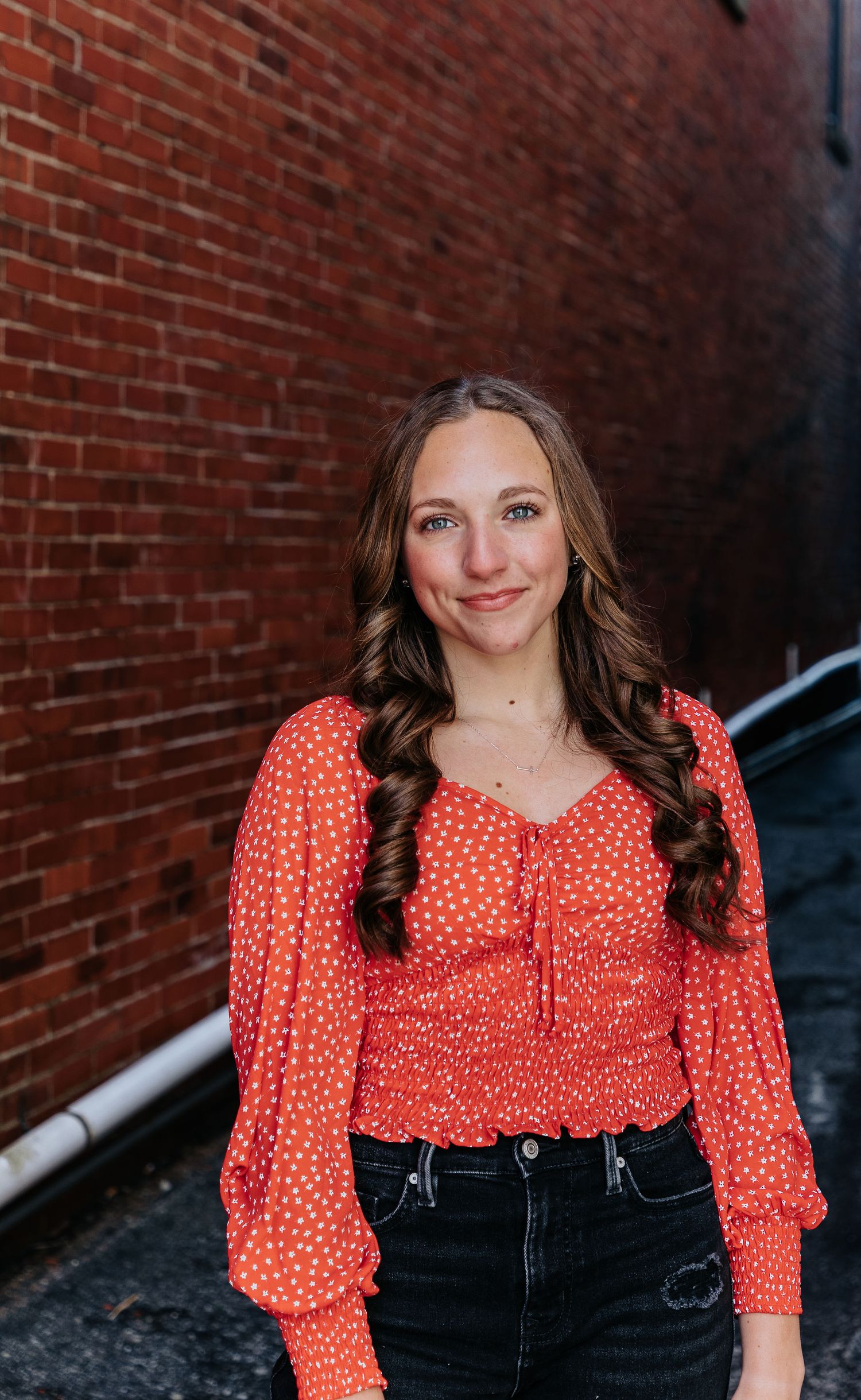 A polka dot red blouse with puff sleeves styled with dark denim jeans against a brick wall background.