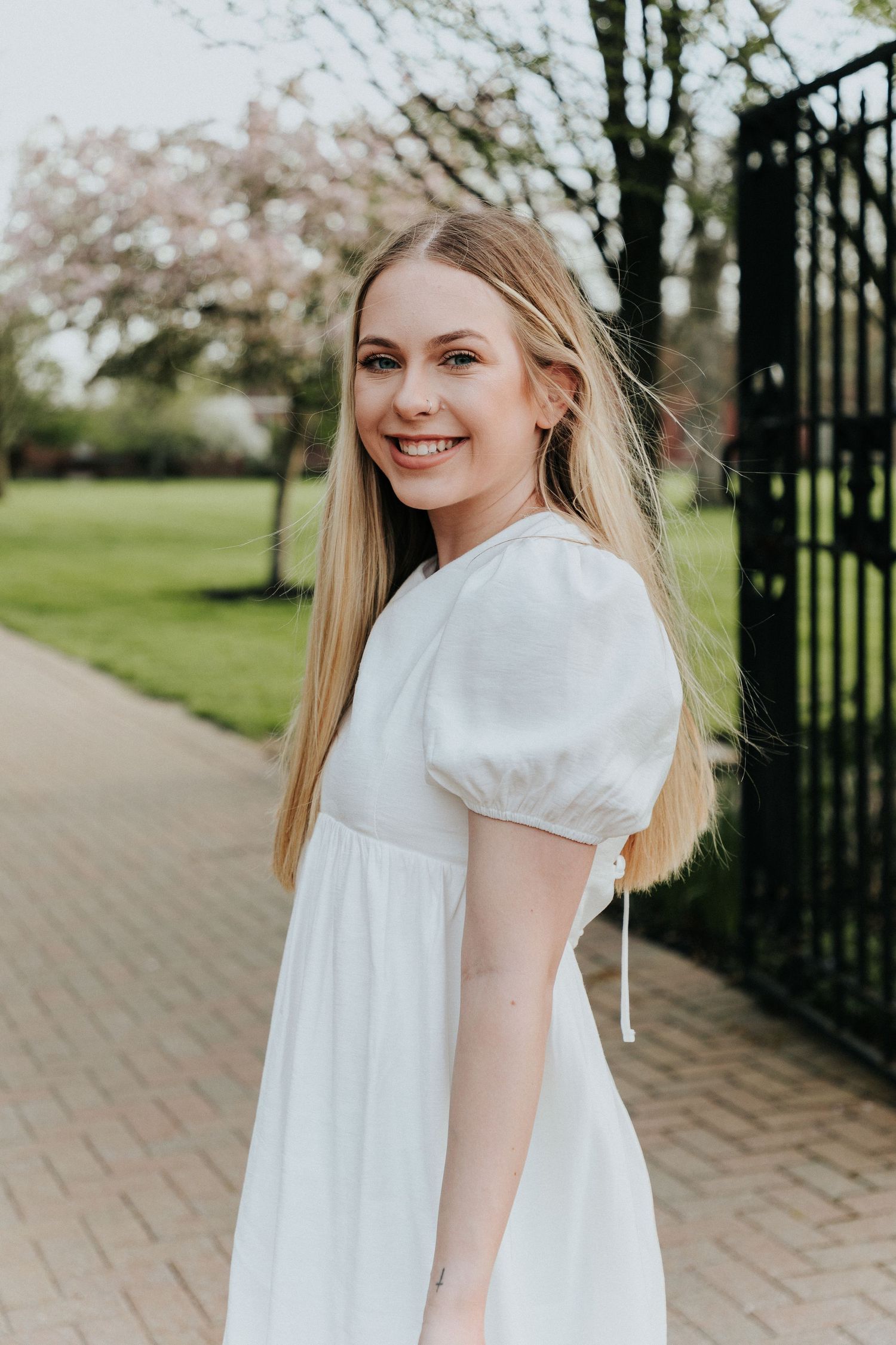 A white puff sleeve dress worn for graduation photos on a brick pathway with spring foliage.