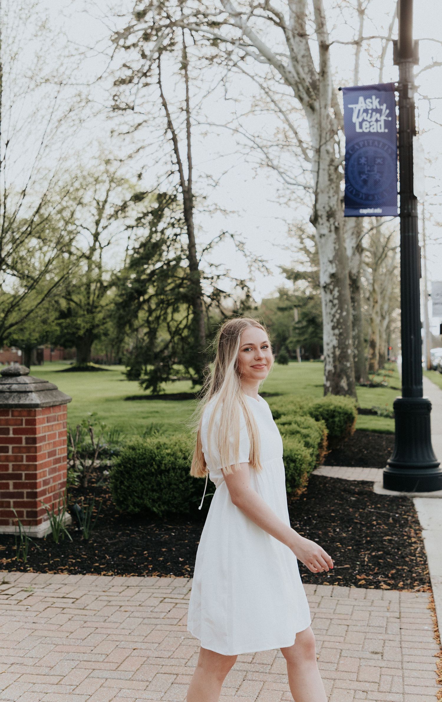 A white spring dress styled for graduation photos on a university campus pathway.