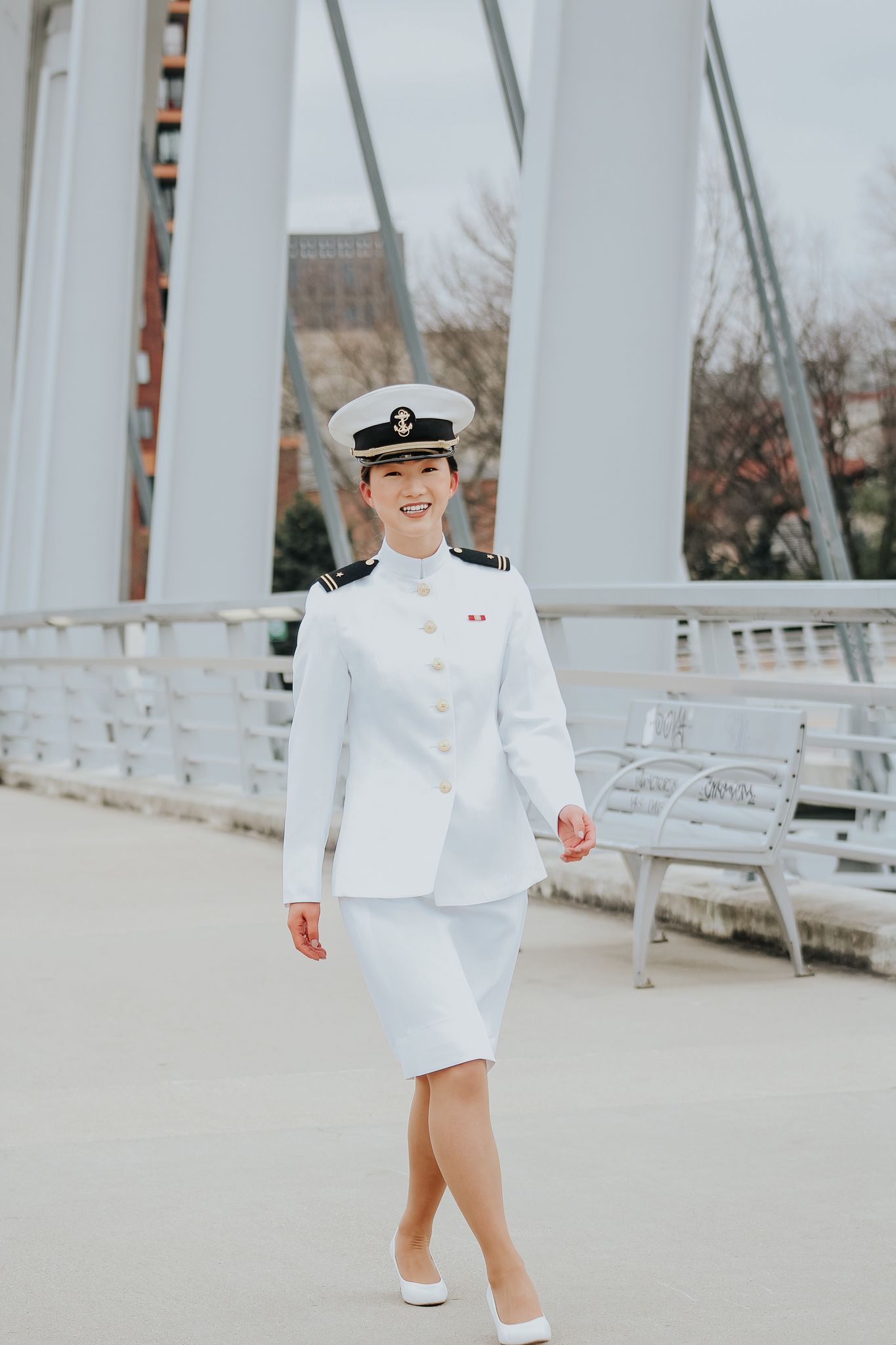A person in crisp white naval uniform and cap stands on a bridge walkway.