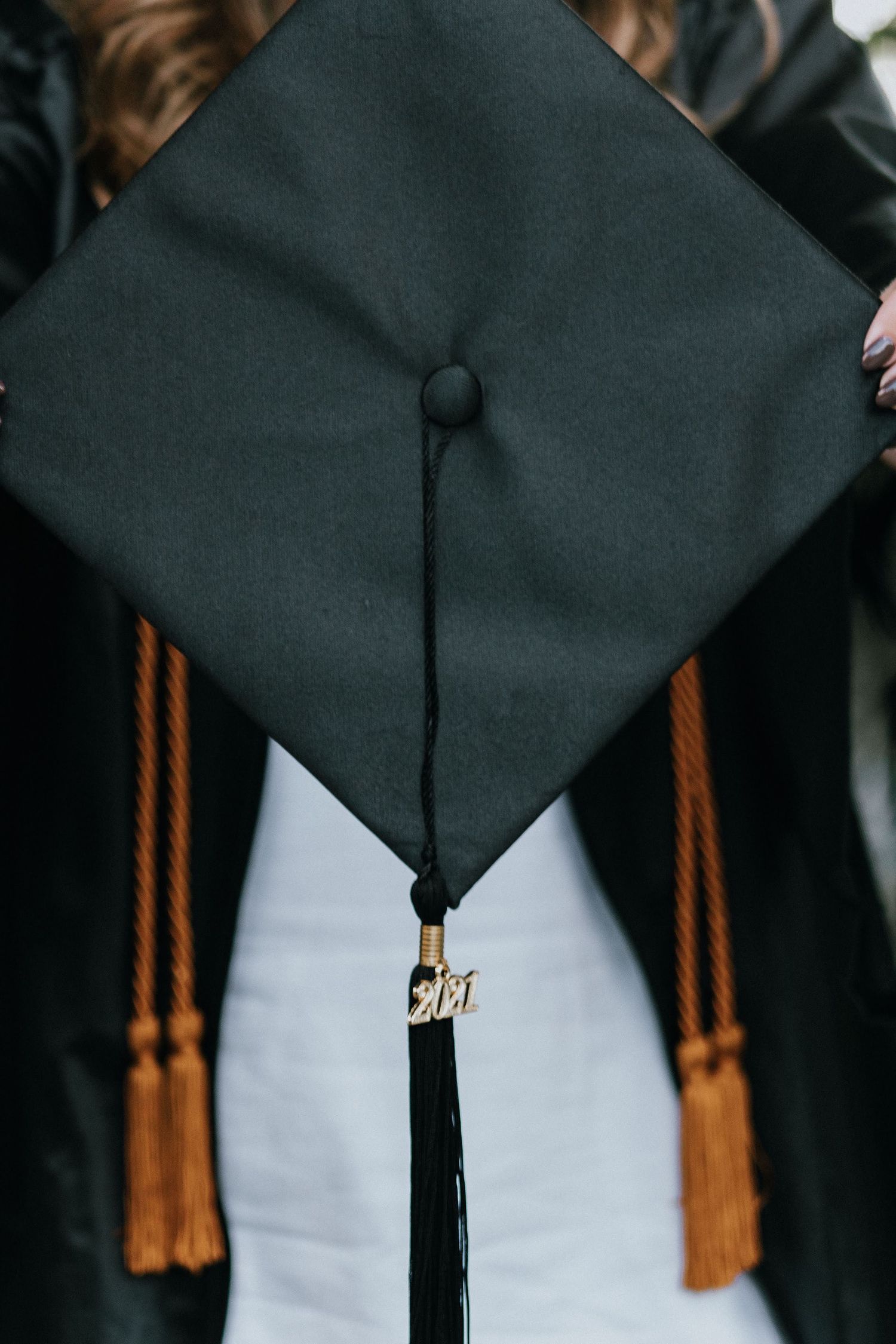Close-up of a black graduation cap with gold tassel against a light background.