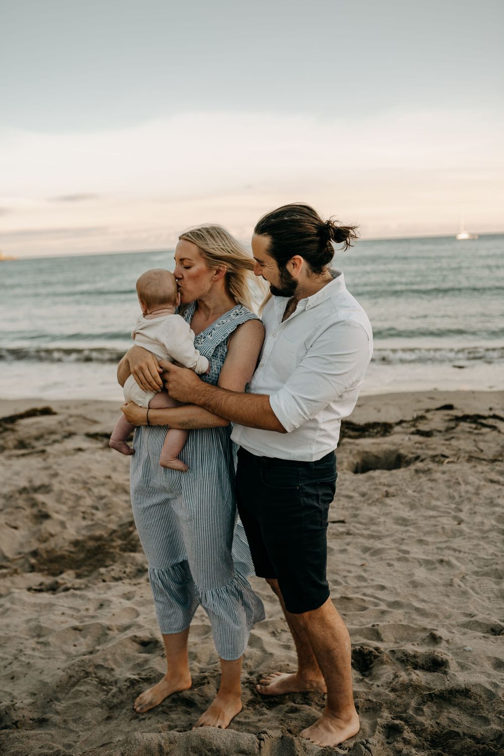 Tender family moment captured on beach at sunset with soft ocean waves in background.