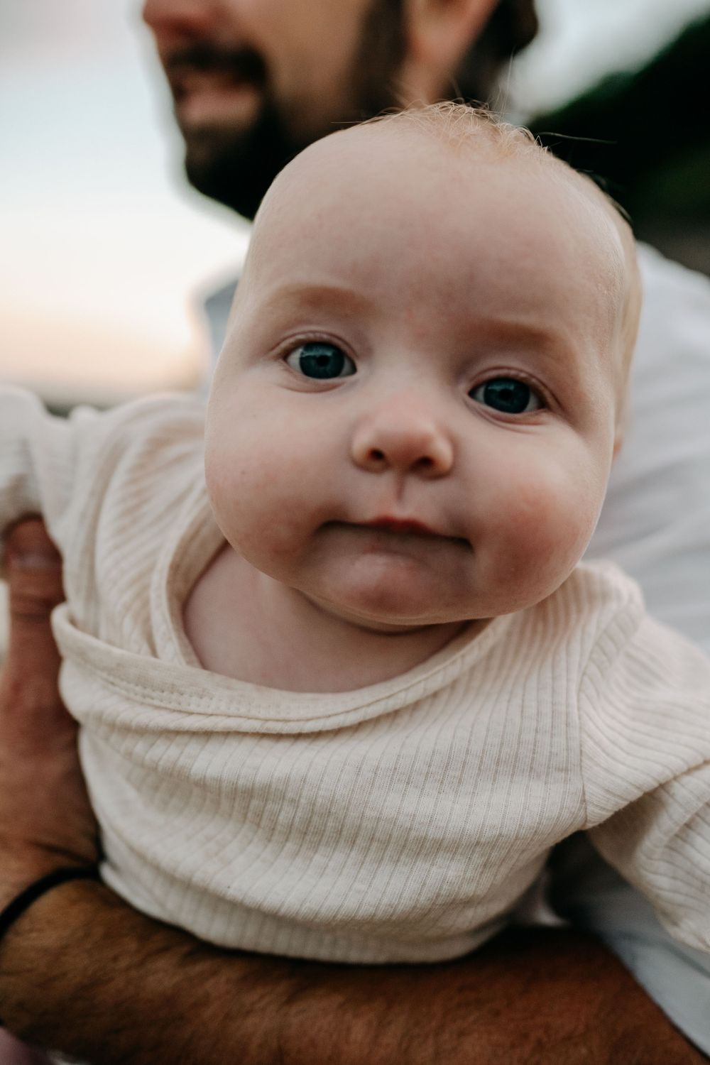 A close-up portrait of an infant wearing a cream-colored sweater.