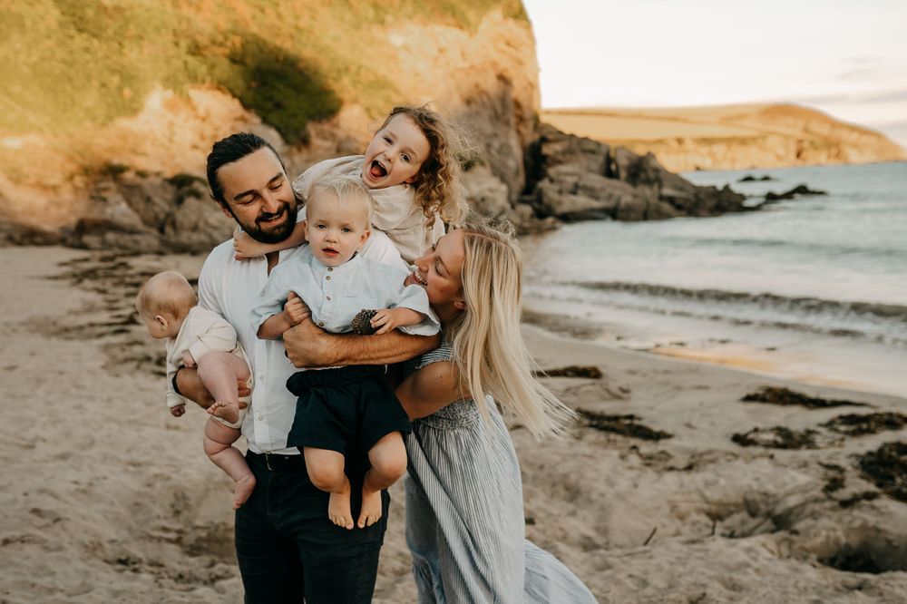 Happy family sharing playful moment on beach with coastal cliffs and ocean views.