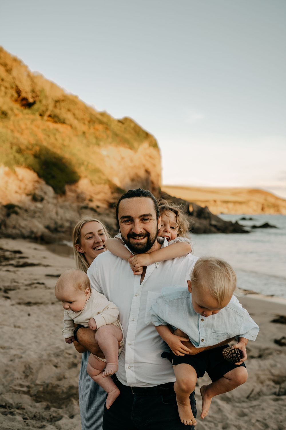 Joyful beach family portrait with dramatic coastal cliffs during golden hour.