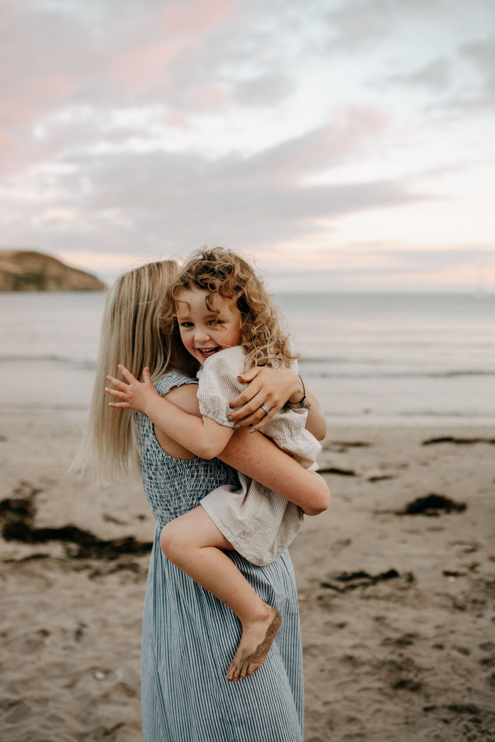 A warm embrace shared between parent and child on a sandy beach at sunset.
