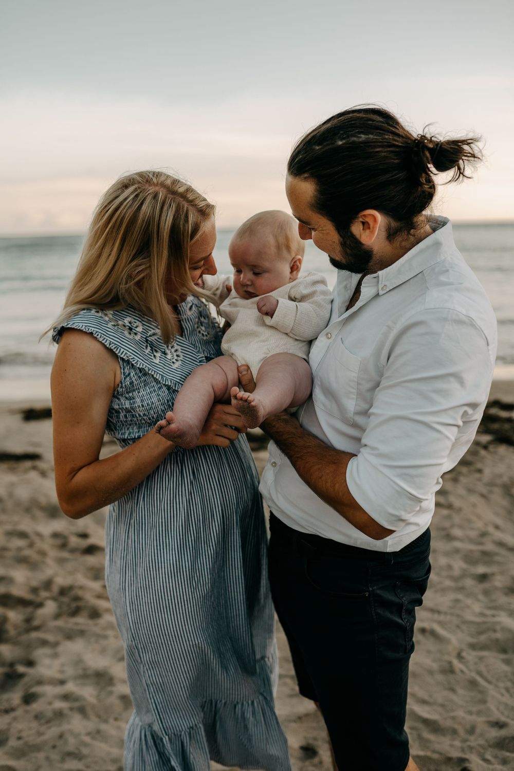 Intimate family moment captured on sandy beach during sunset.