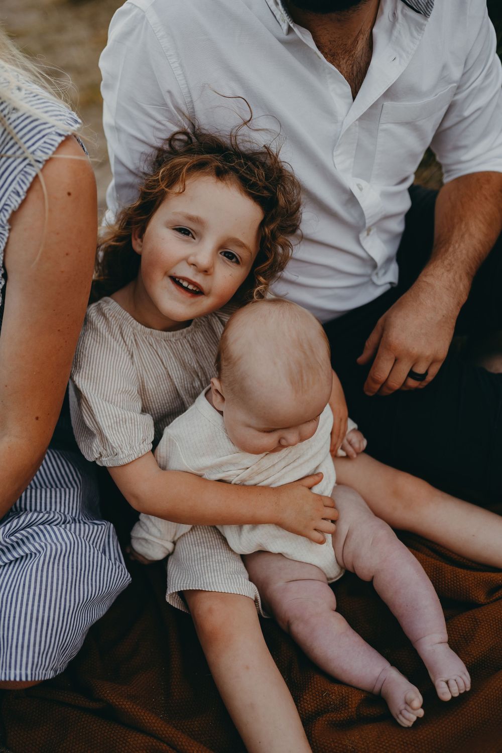 Two siblings share a tender moment sitting together on a blanket outdoors.