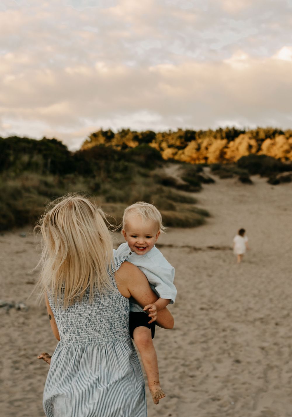 Parent and child share a joyful moment on beach path during golden hour.