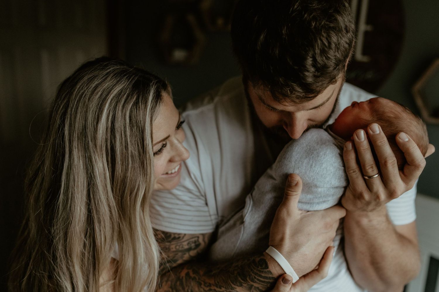Parents tenderly holding their newborn baby in dimly lit room.