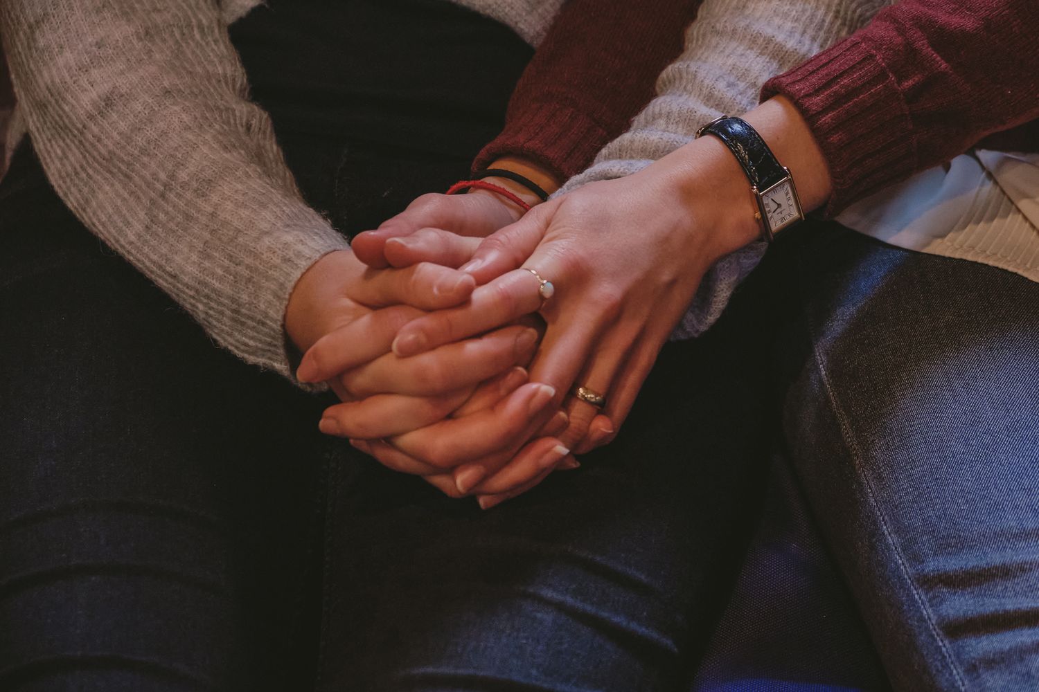 Close-up of hands clasped together while sitting on a bench.