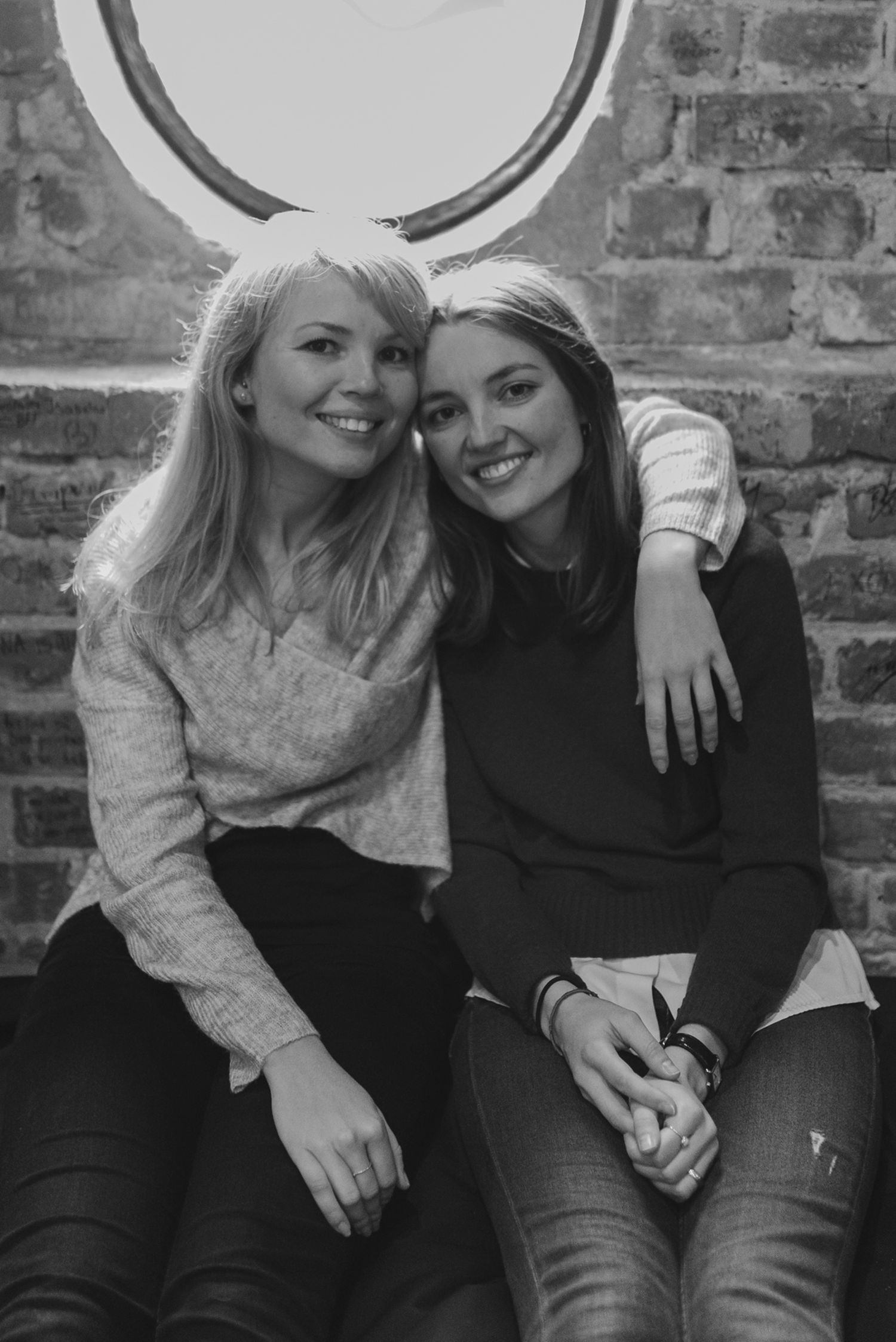 Two friends sharing a candid moment on a brick wall bench.