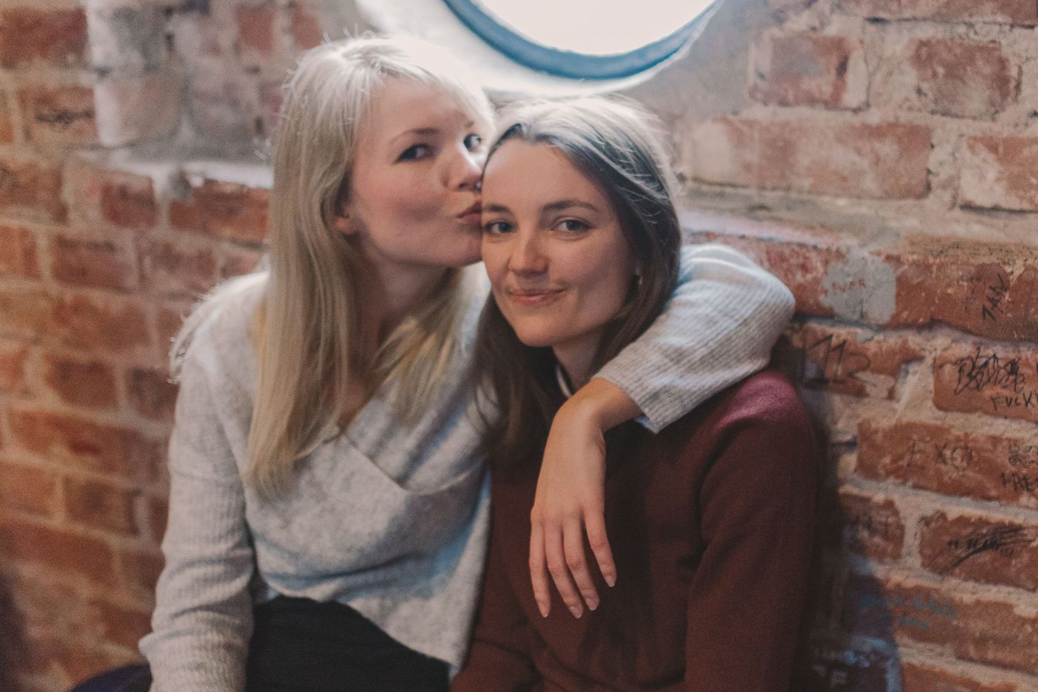 Casual friends relaxing against exposed brick wall during indoor photoshoot.