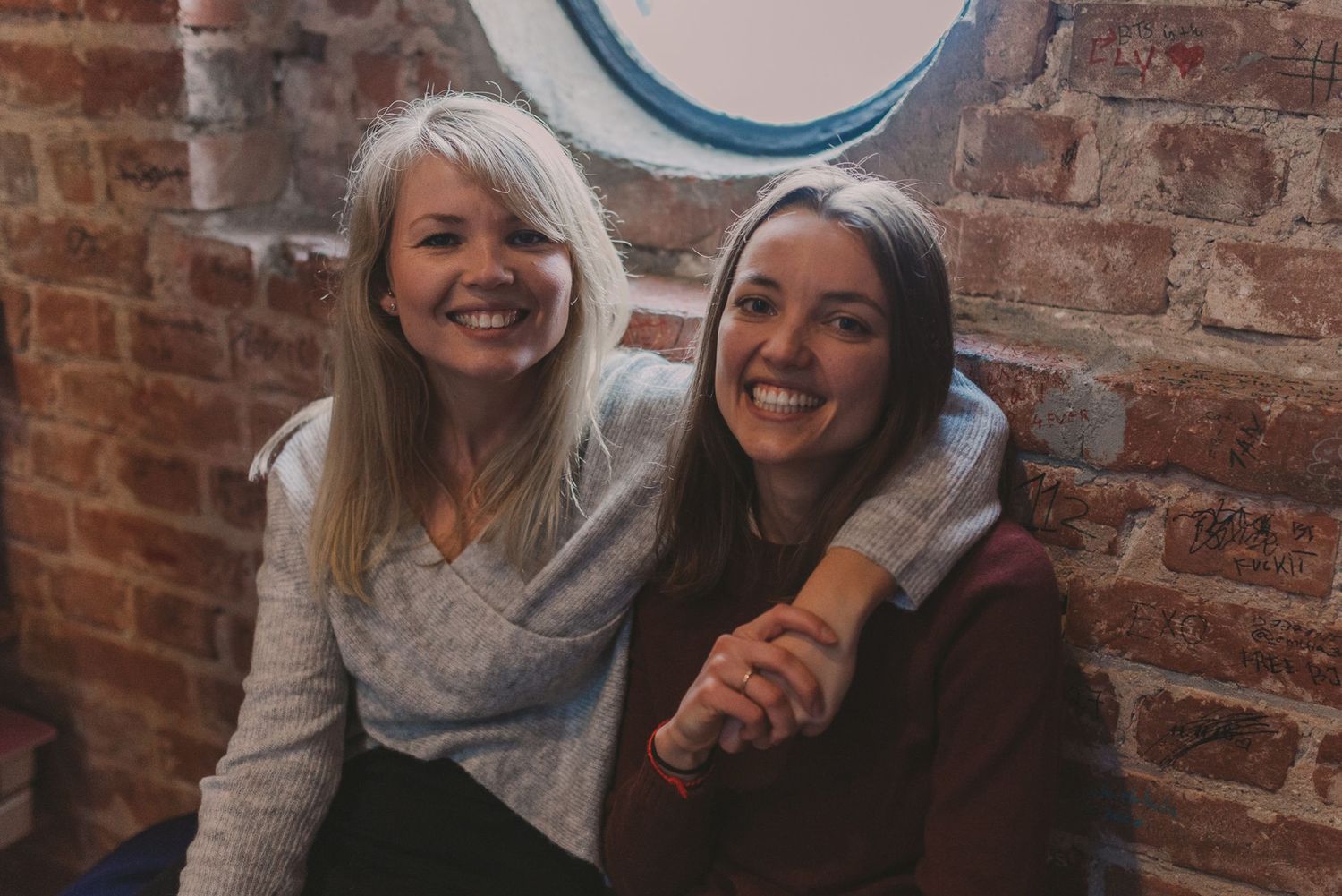 Candid moment of friendship captured against rustic brick wall background.