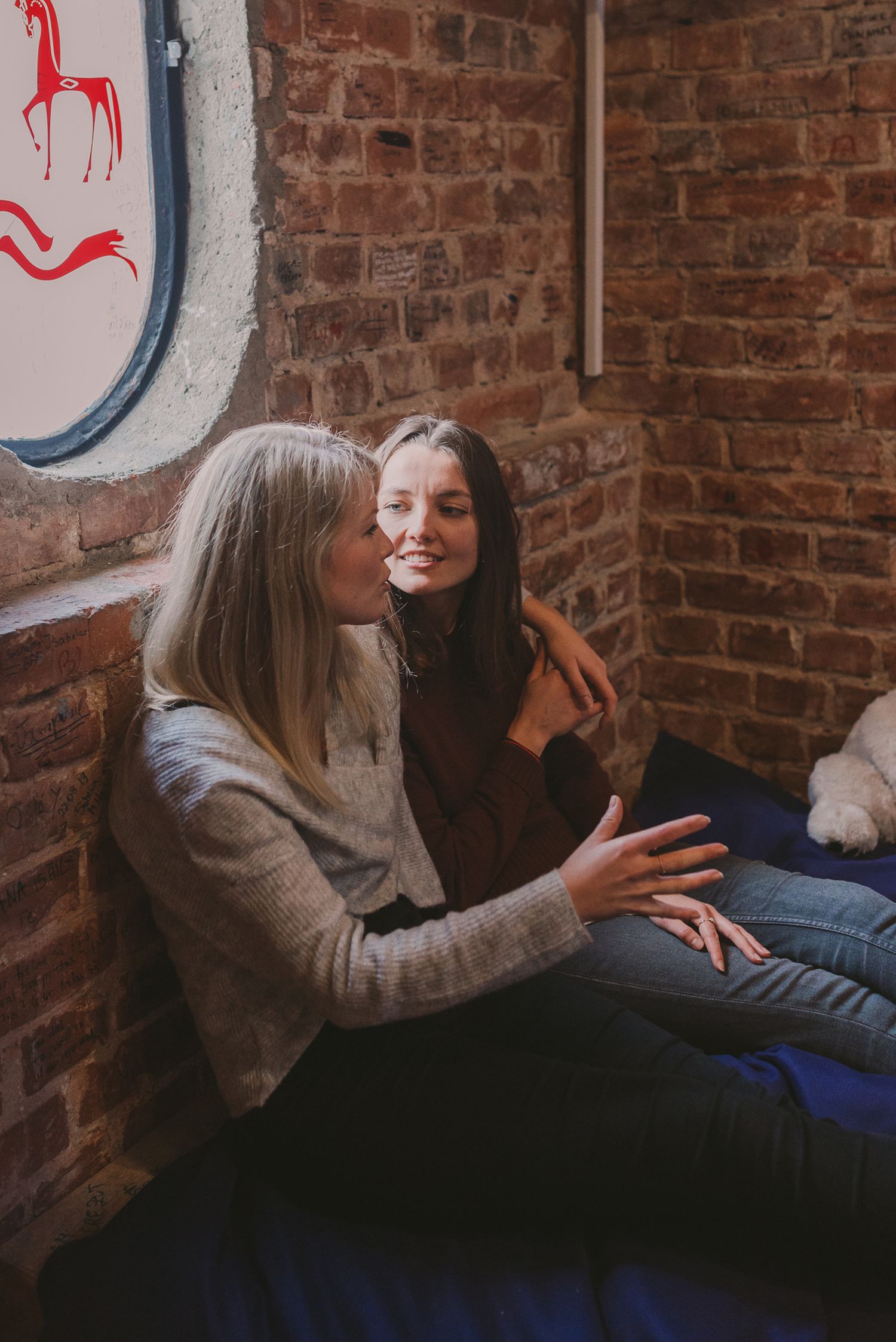 Friends sharing laughter while lounging against brick wall with artistic details.
