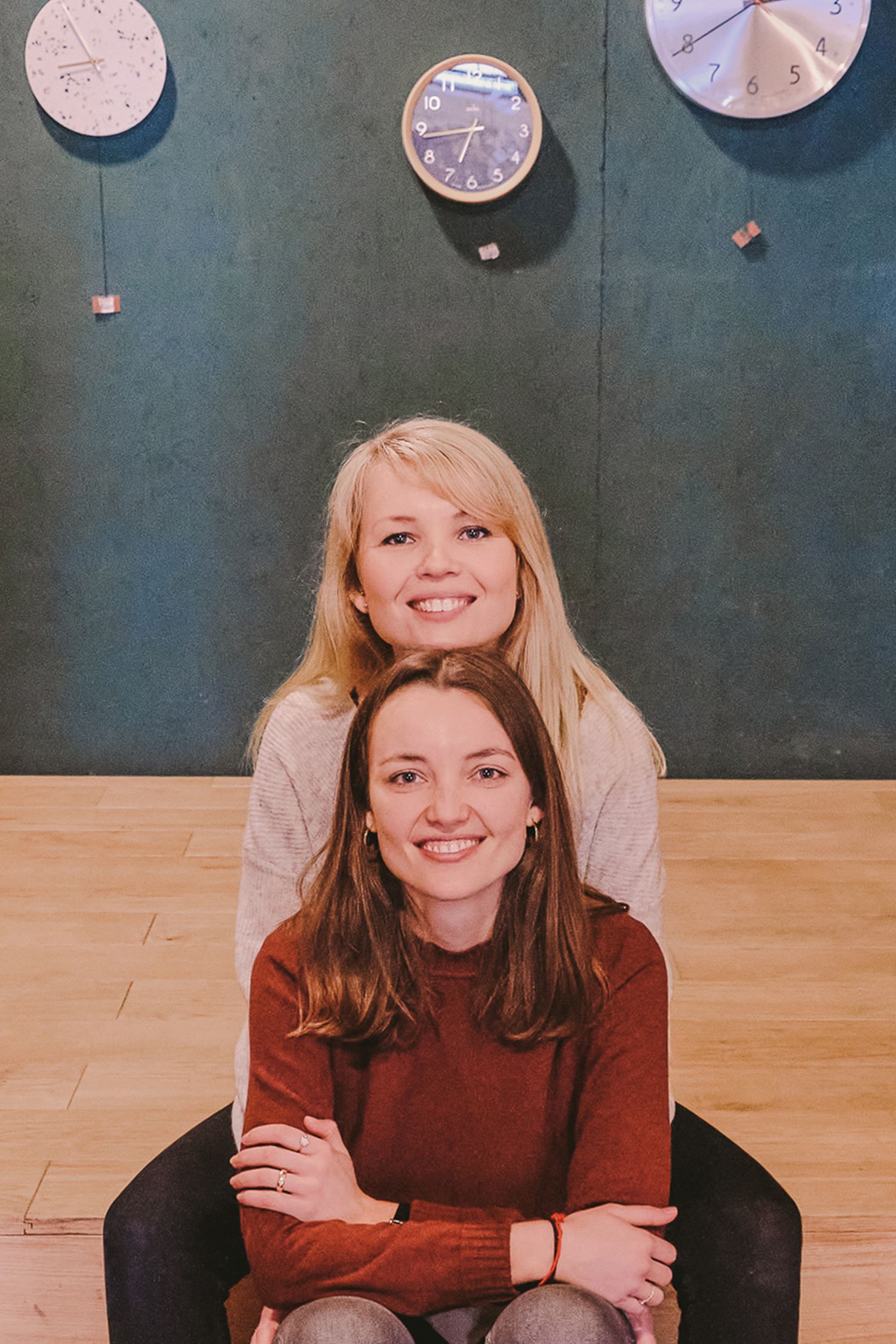 Two friends share joyful moments together in a room with clocks on the wall.