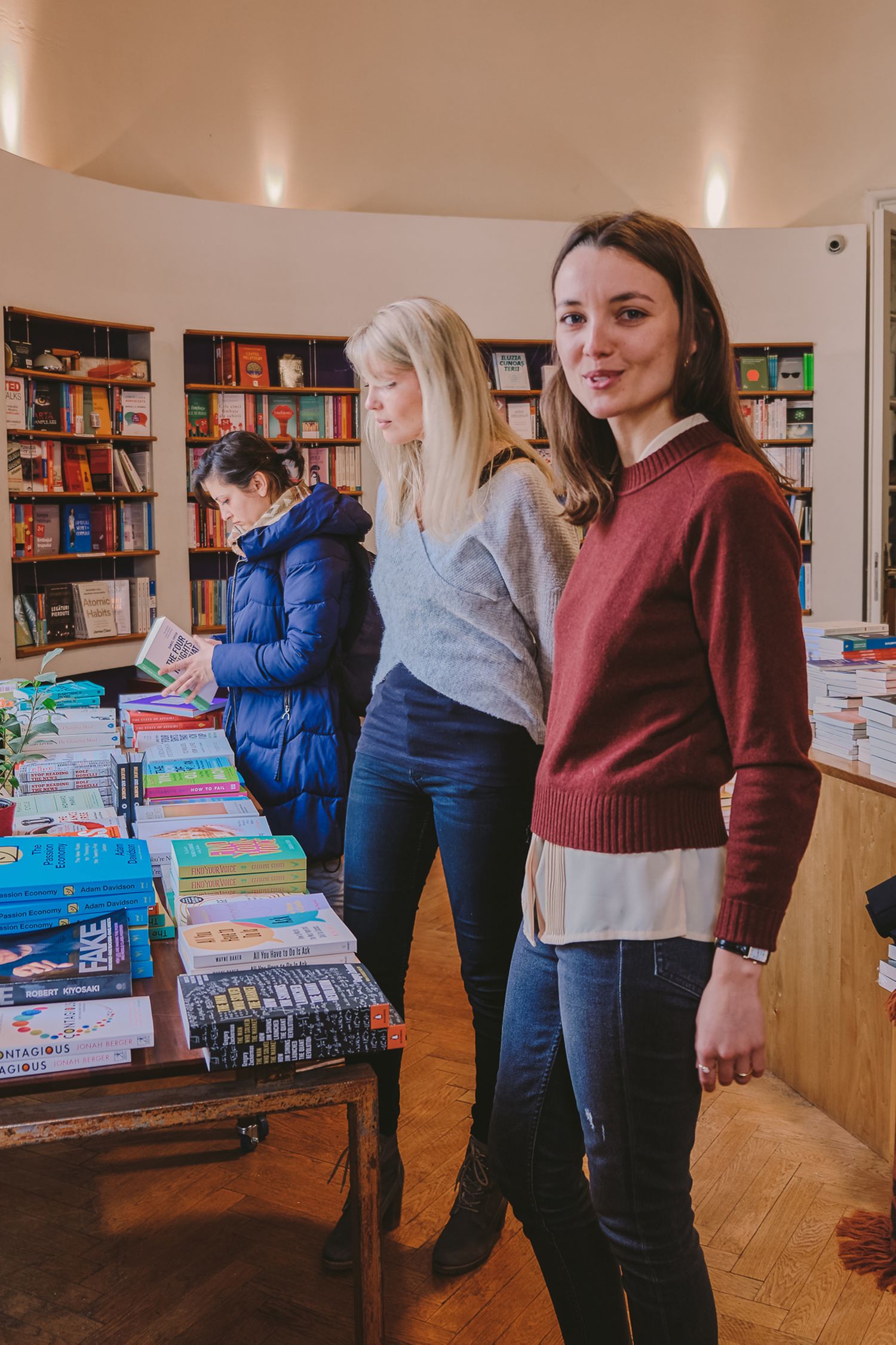 Friends browsing books together in a sunlit library room with hardwood floors.