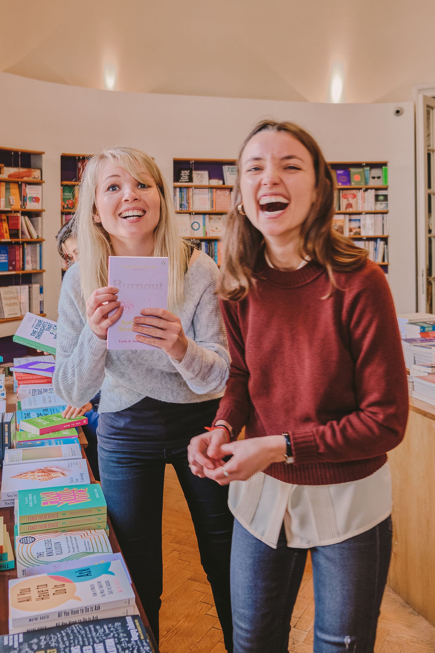 Two people sharing laughs while looking through books in a bright library space.