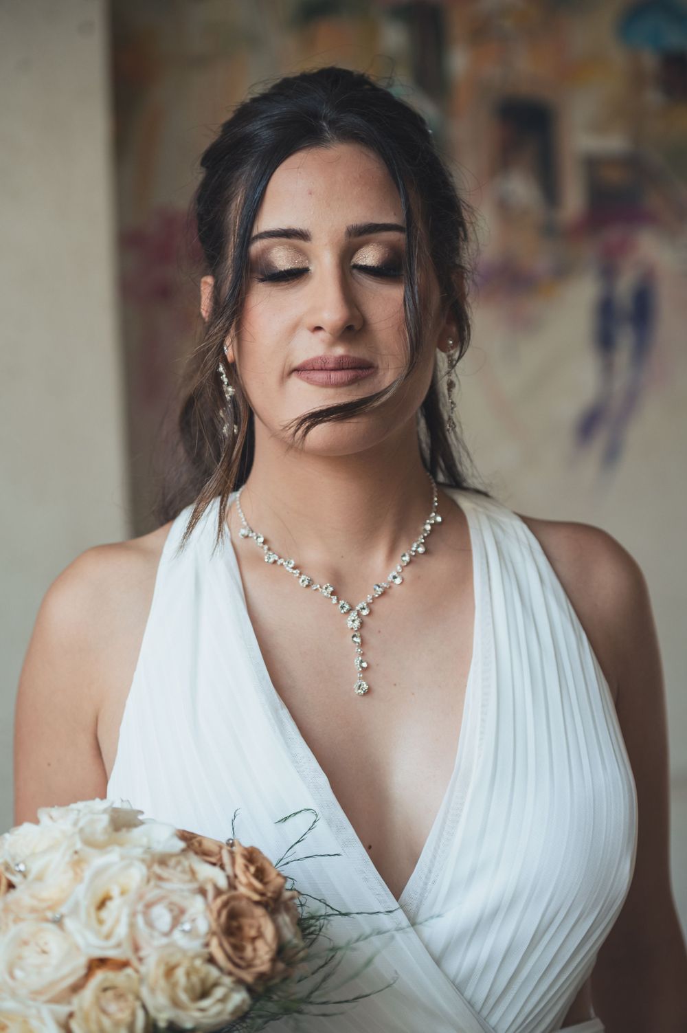 A bride in a white dress holding cream roses with delicate jewelry and elegant makeup.