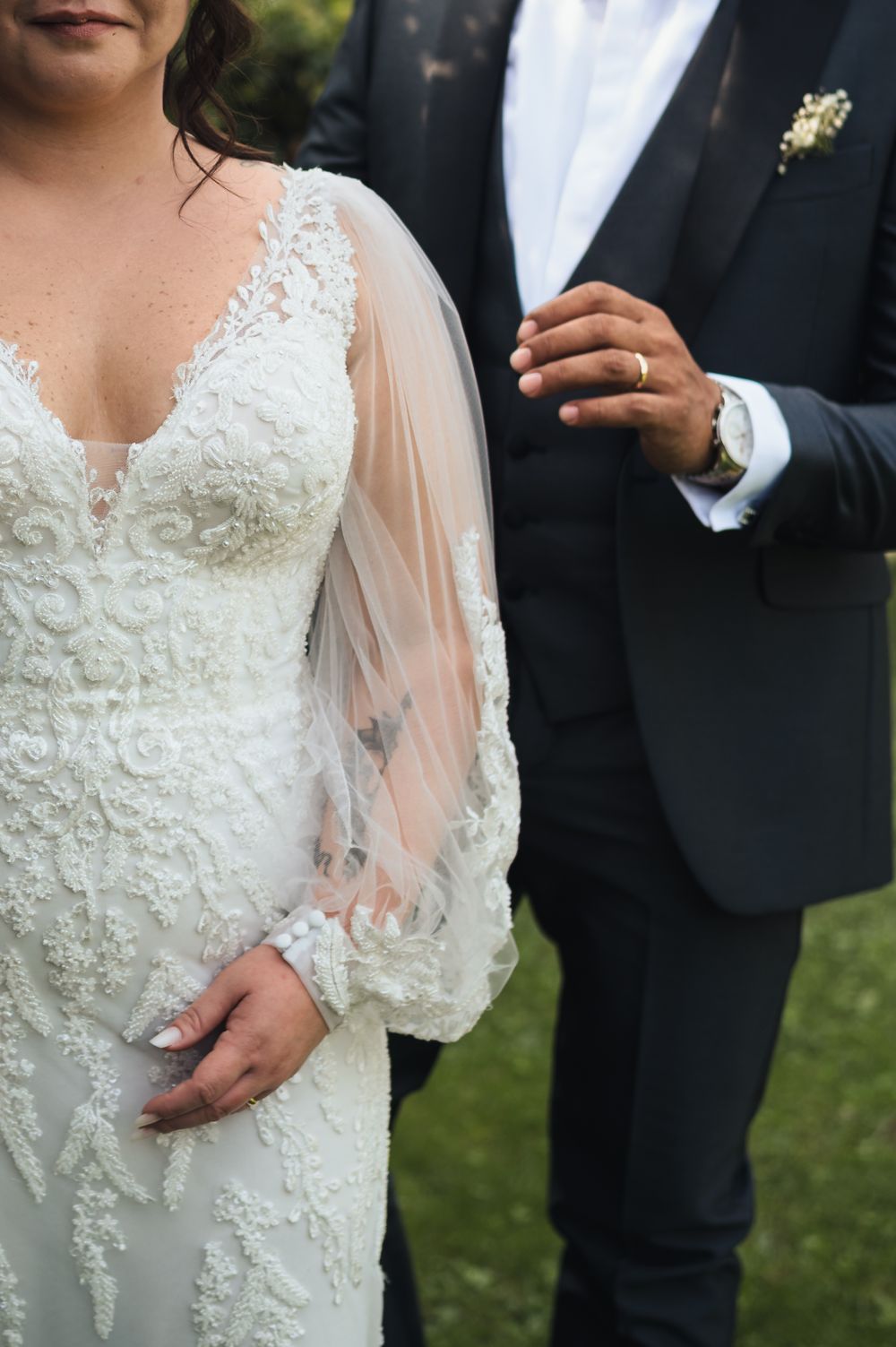 Detail shot of intricate lace wedding dress sleeve and dark suit jacket.