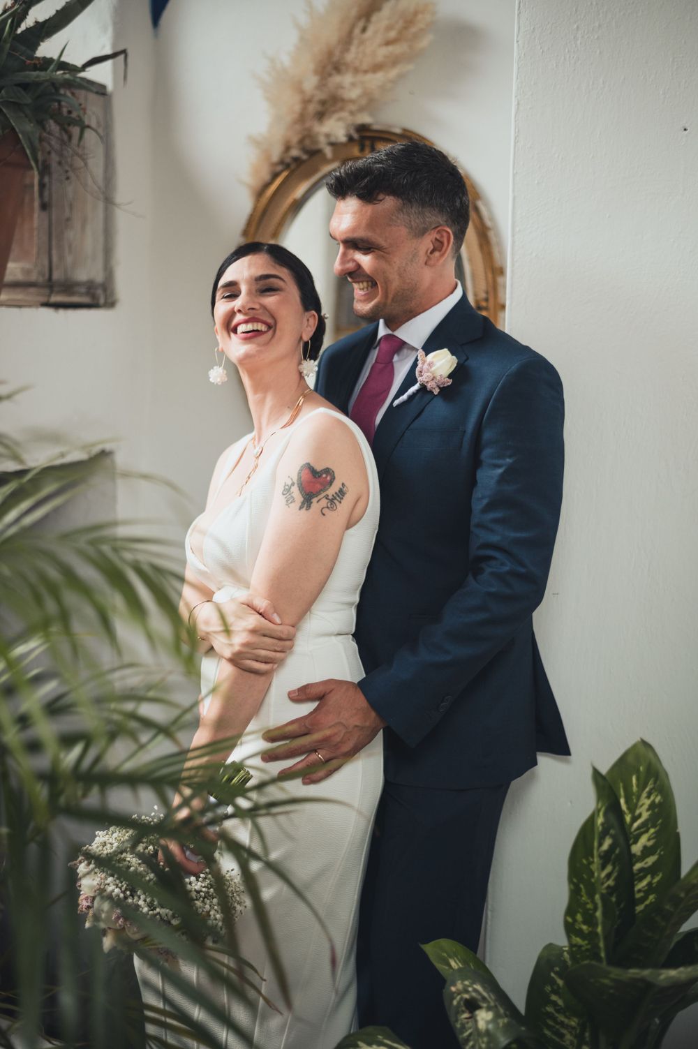 A joyful moment captured between a couple against a white wall with dried pampas grass decor.