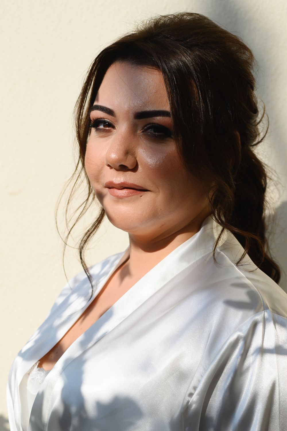 Close-up portrait of woman in white silk robe with elegant makeup and updo hairstyle.