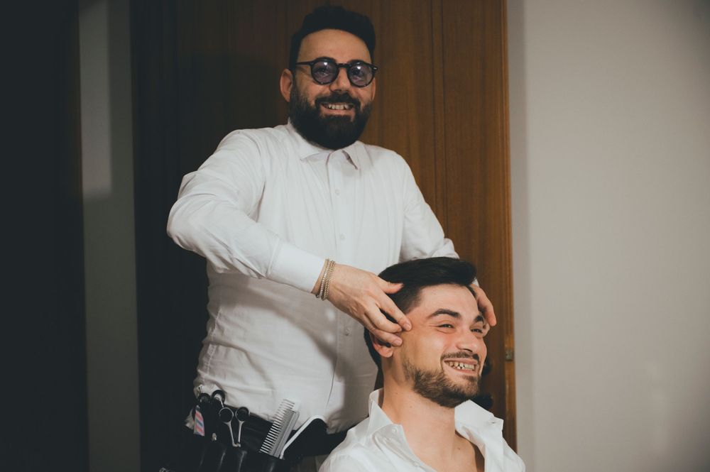 Smiling barber styling groom's hair during wedding morning preparation.