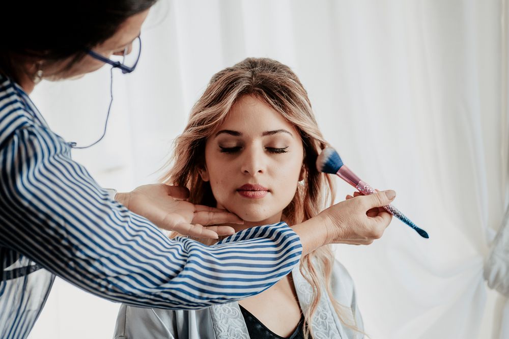 Professional stylist working on hair and makeup during a beauty session in a bright room.