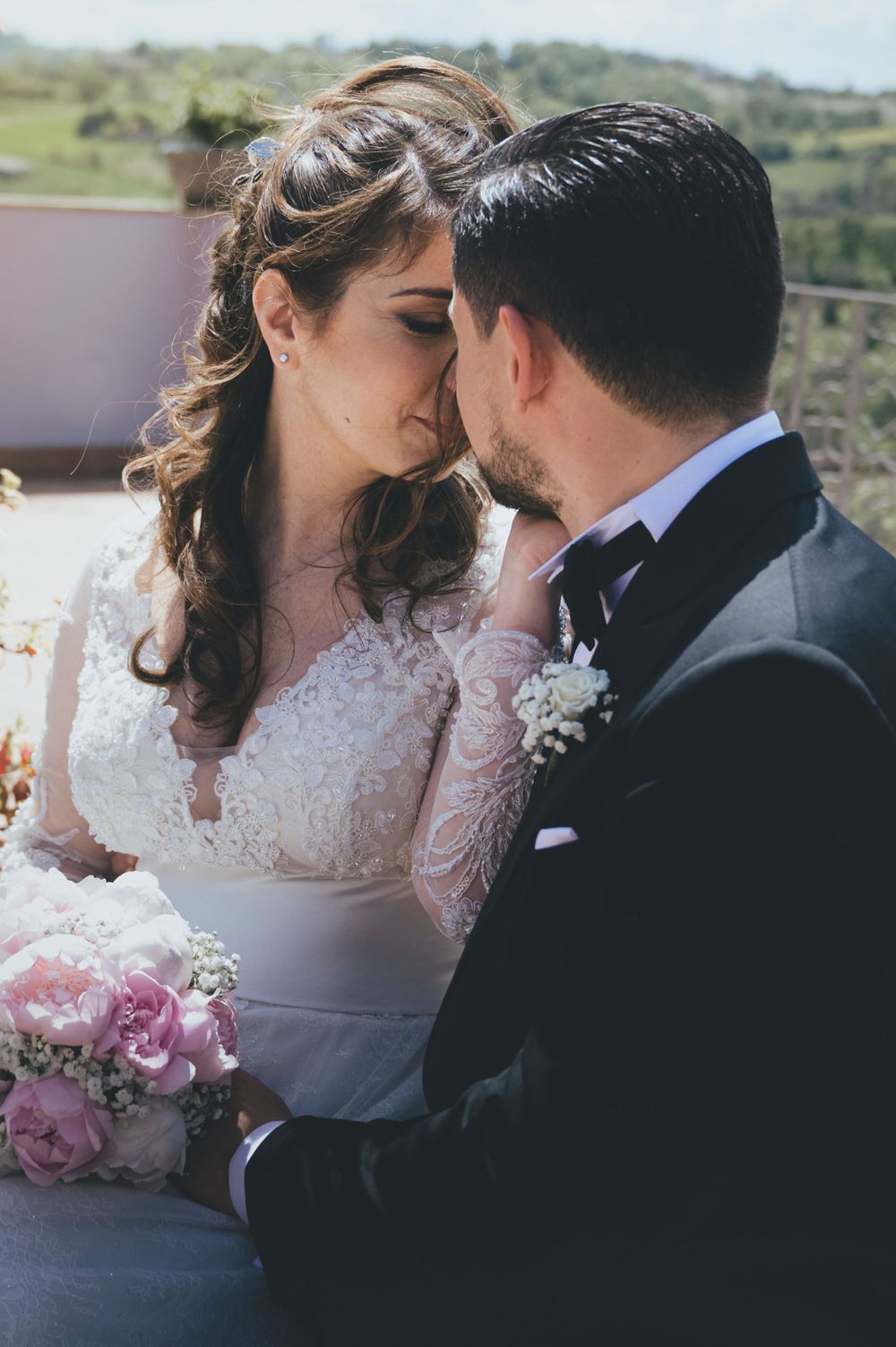 Bride and groom sharing an intimate moment, bride in lace gown holding pink roses bouquet.