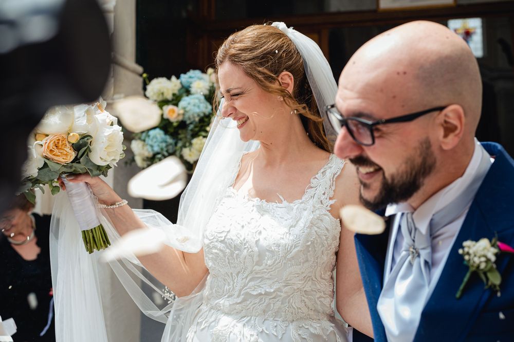Happy bride in lace wedding dress laughing with groom after ceremony with confetti.
