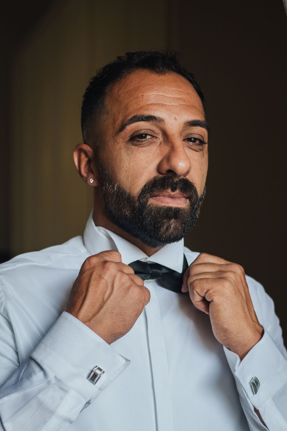 Person in white dress shirt adjusting black bowtie while preparing for formal event.