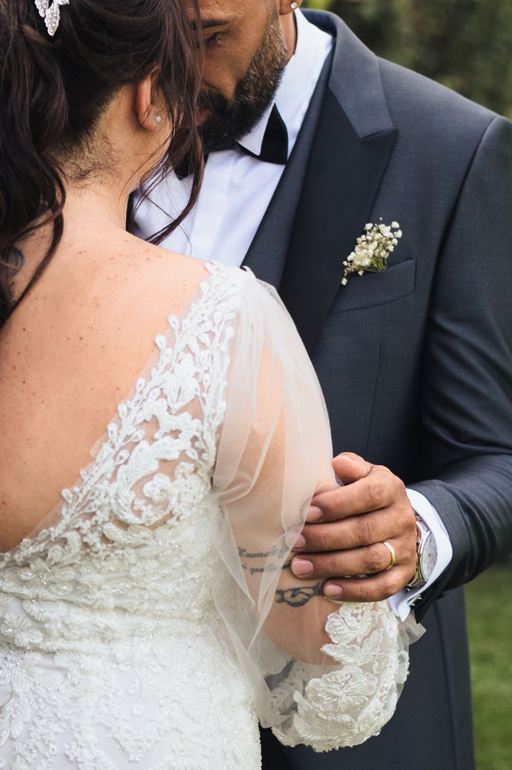 Close-up detail of lace wedding dress and formal suit during intimate moment.