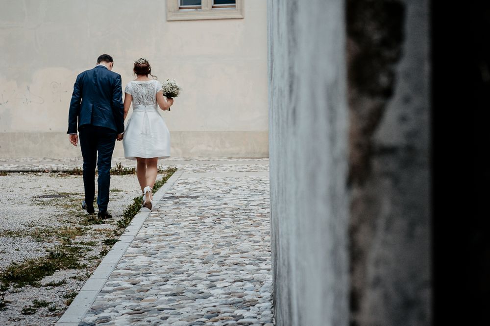 A couple walks hand in hand down a cobblestone path in wedding attire.