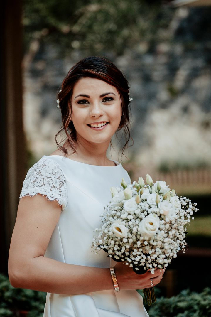 A bridal portrait featuring a simple white dress and bouquet of white flowers against a natural backdrop.
