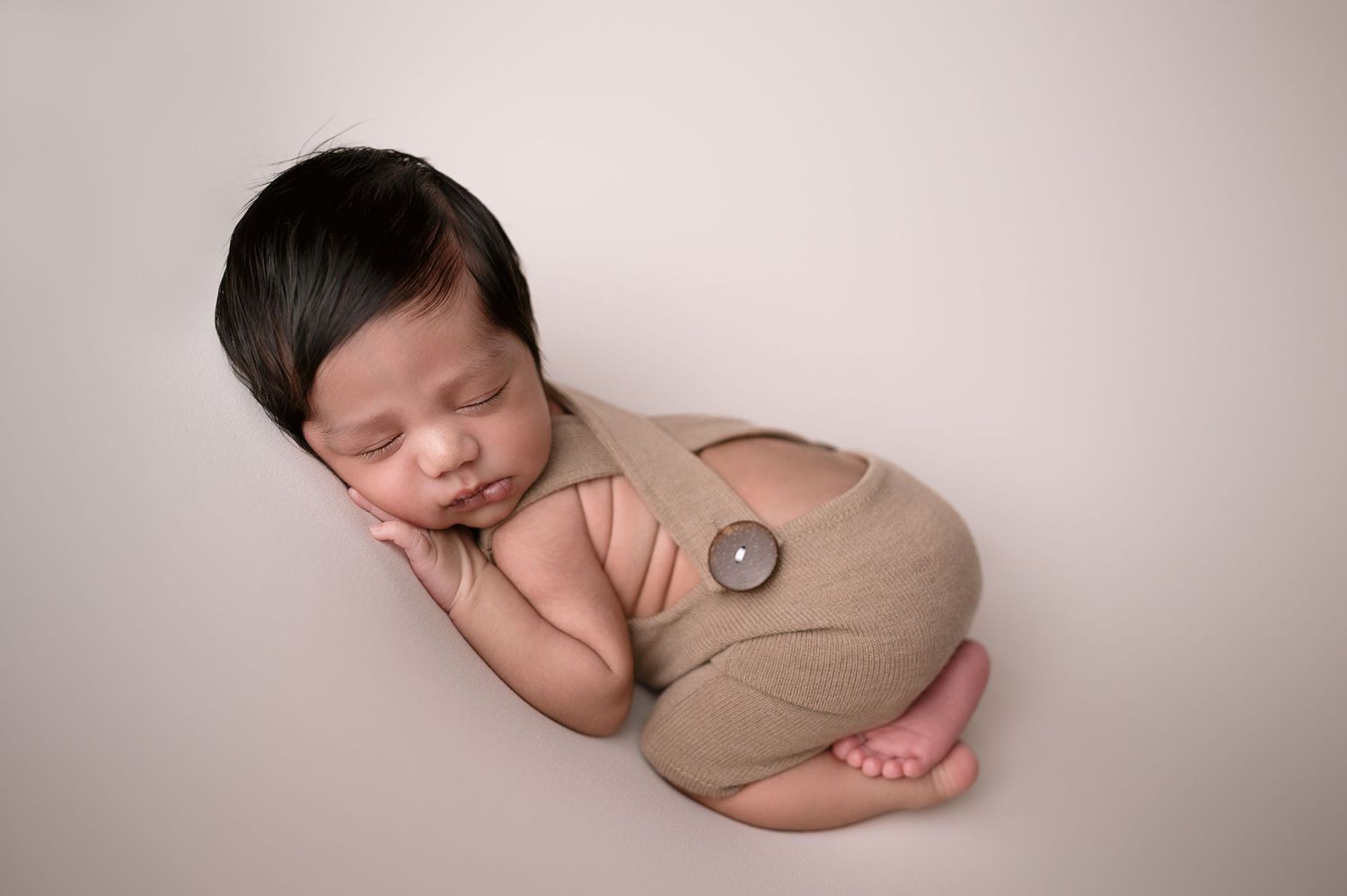 Professional newborn portraits with baby posed in neutral brown wrap on light backdrop.