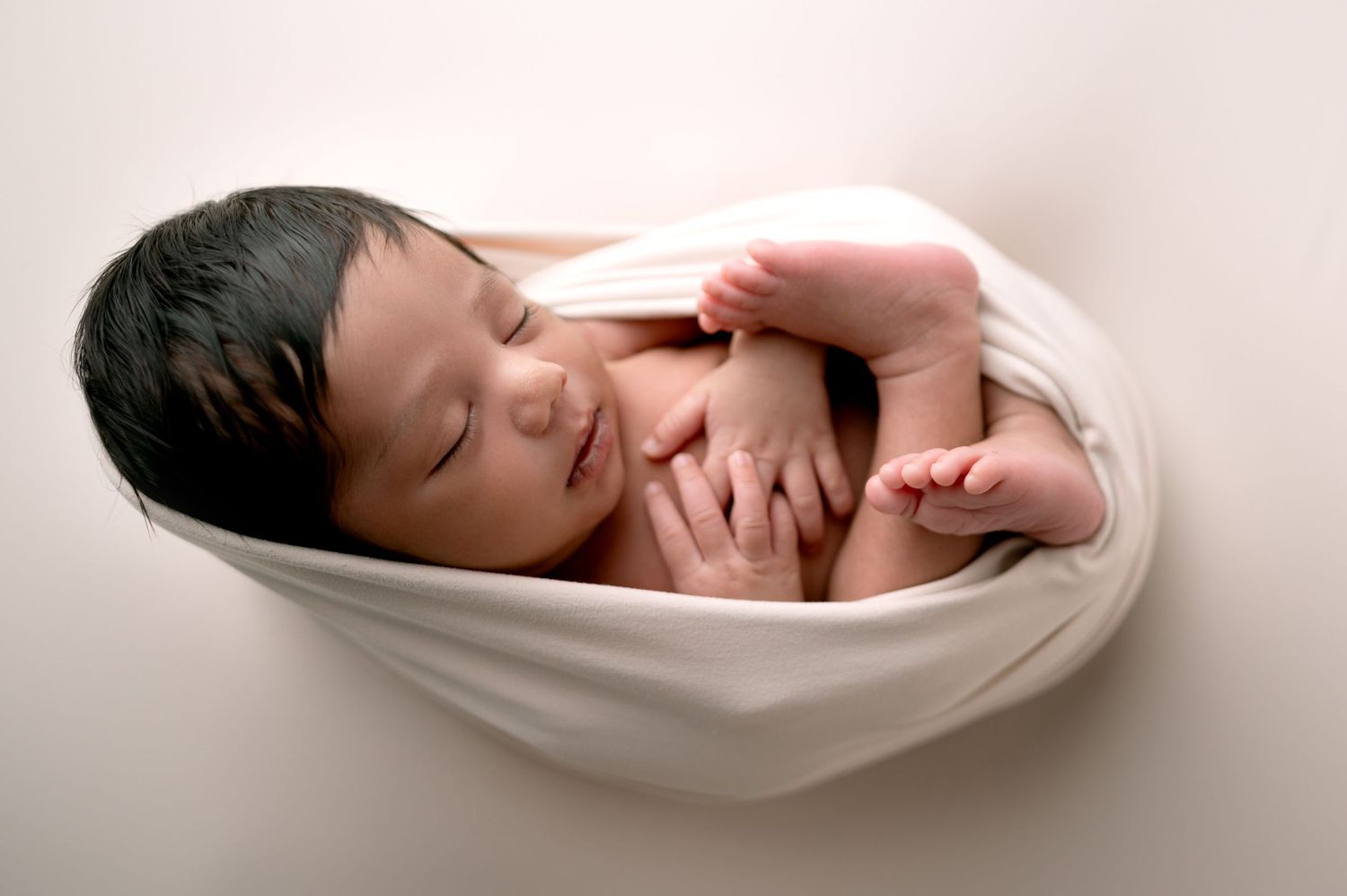Serene sleeping newborn wrapped in white fabric against minimalist backdrop.