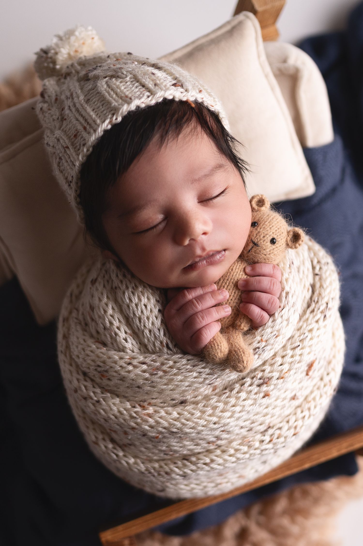 Artistic newborn portraits with baby wrapped in cream knit on dark wood surface.