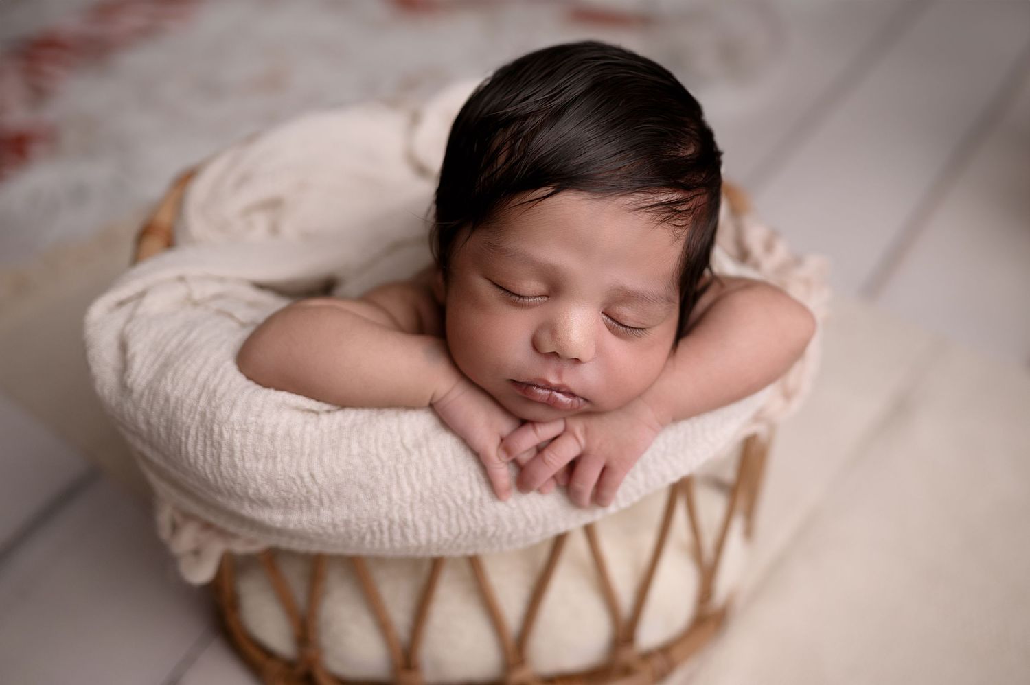 Sleeping newborn resting in white woven basket against light background.