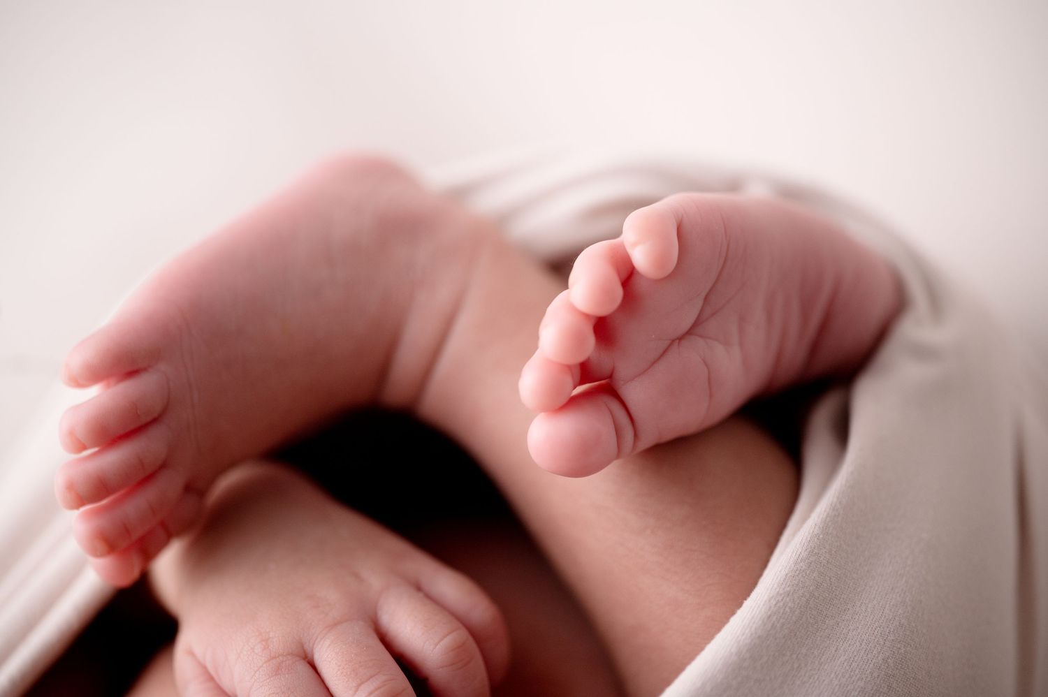 Artistic macro shot of newborn baby feet and toes wrapped in white fabric.