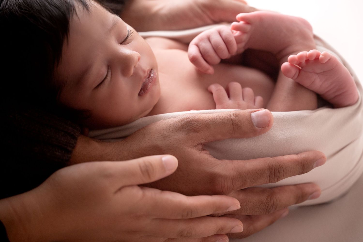 Intimate newborn photography with gentle hands supporting sleeping baby.