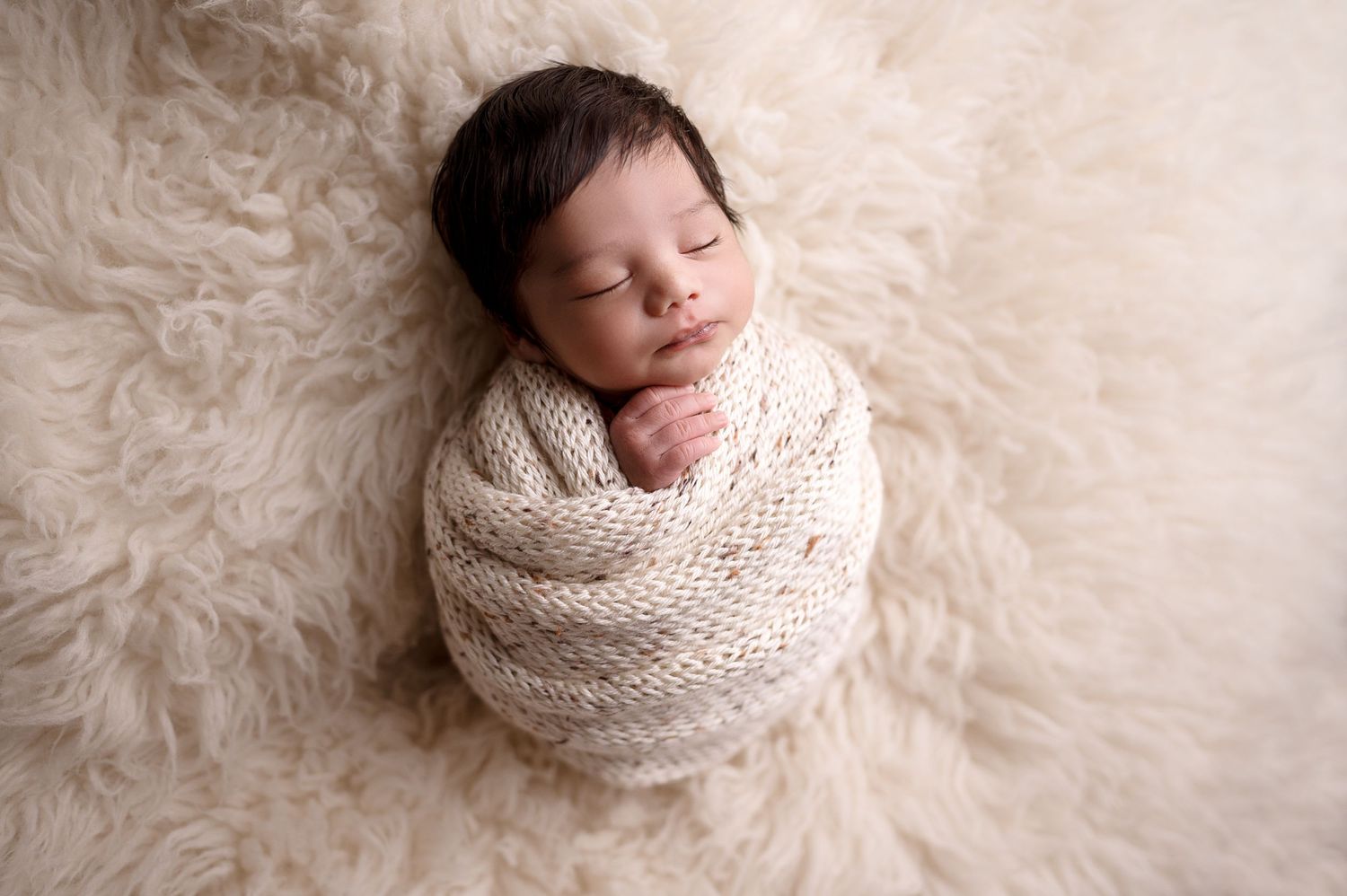 Newborn photography series showing baby wrapped in cream knit on furry white rug.