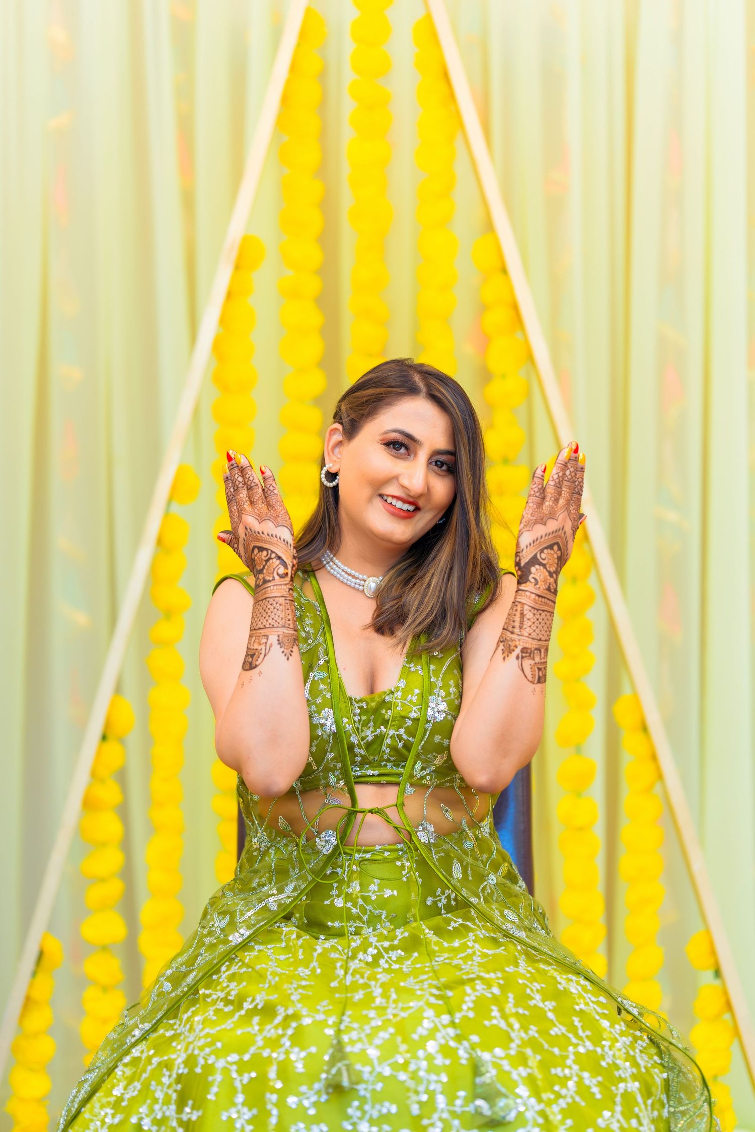 Traditional bridal portrait showing decorated hands against yellow and green backdrop.