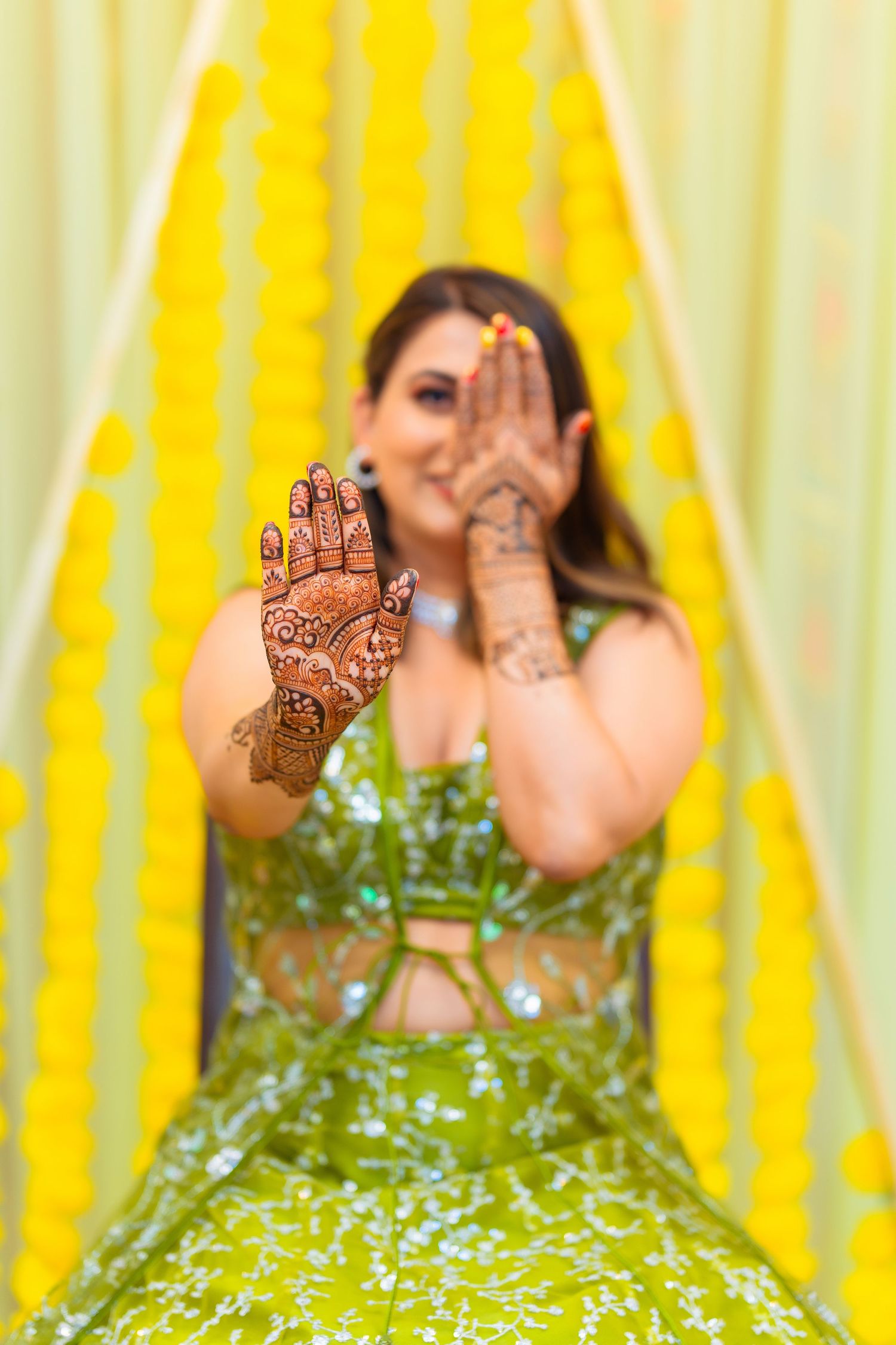 Close up of intricate henna designs on hands with green and yellow background.